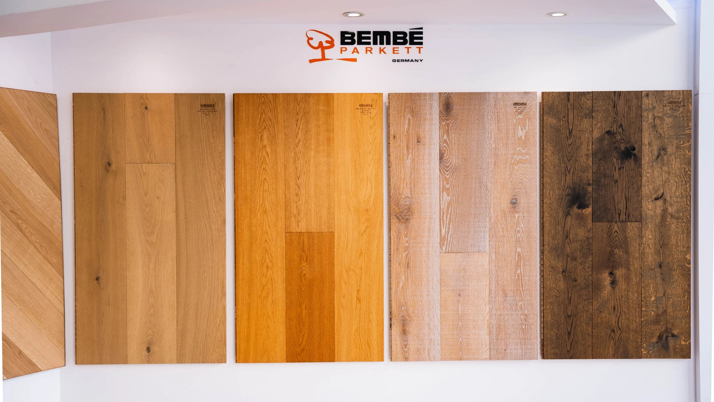 Display of five wooden flooring samples in shades from light to dark, mounted on a white wall with a 'BEMBÉ PARKETT GERMANY' logo above them.