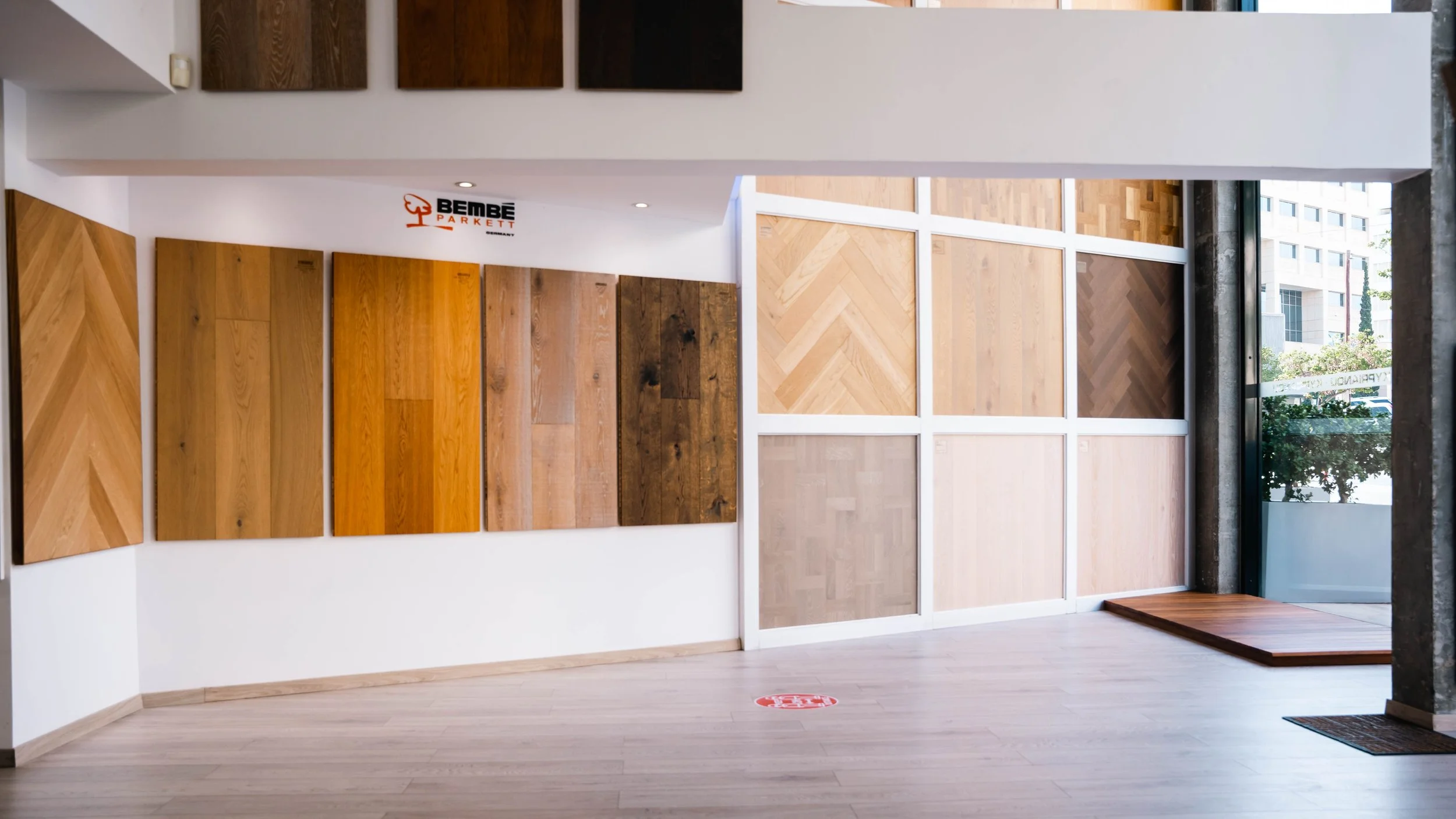 Display of various wood flooring samples arranged on a wall in a showroom with a large window letting in natural light.