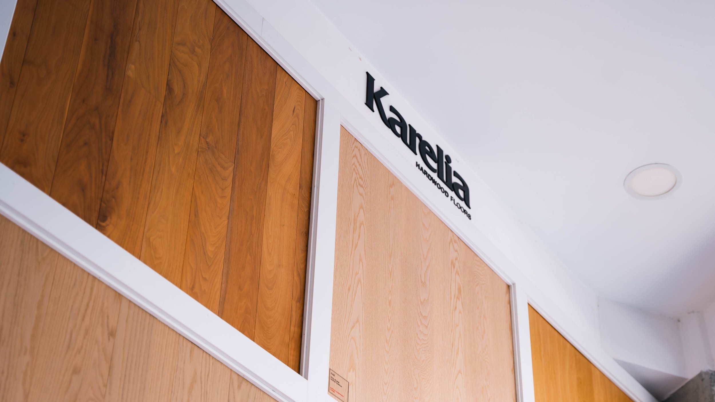 Display of various hardwood flooring samples on the wall at a flooring store, with the store's name 'karelia HARDWOOD FLOORS' visible nearby.