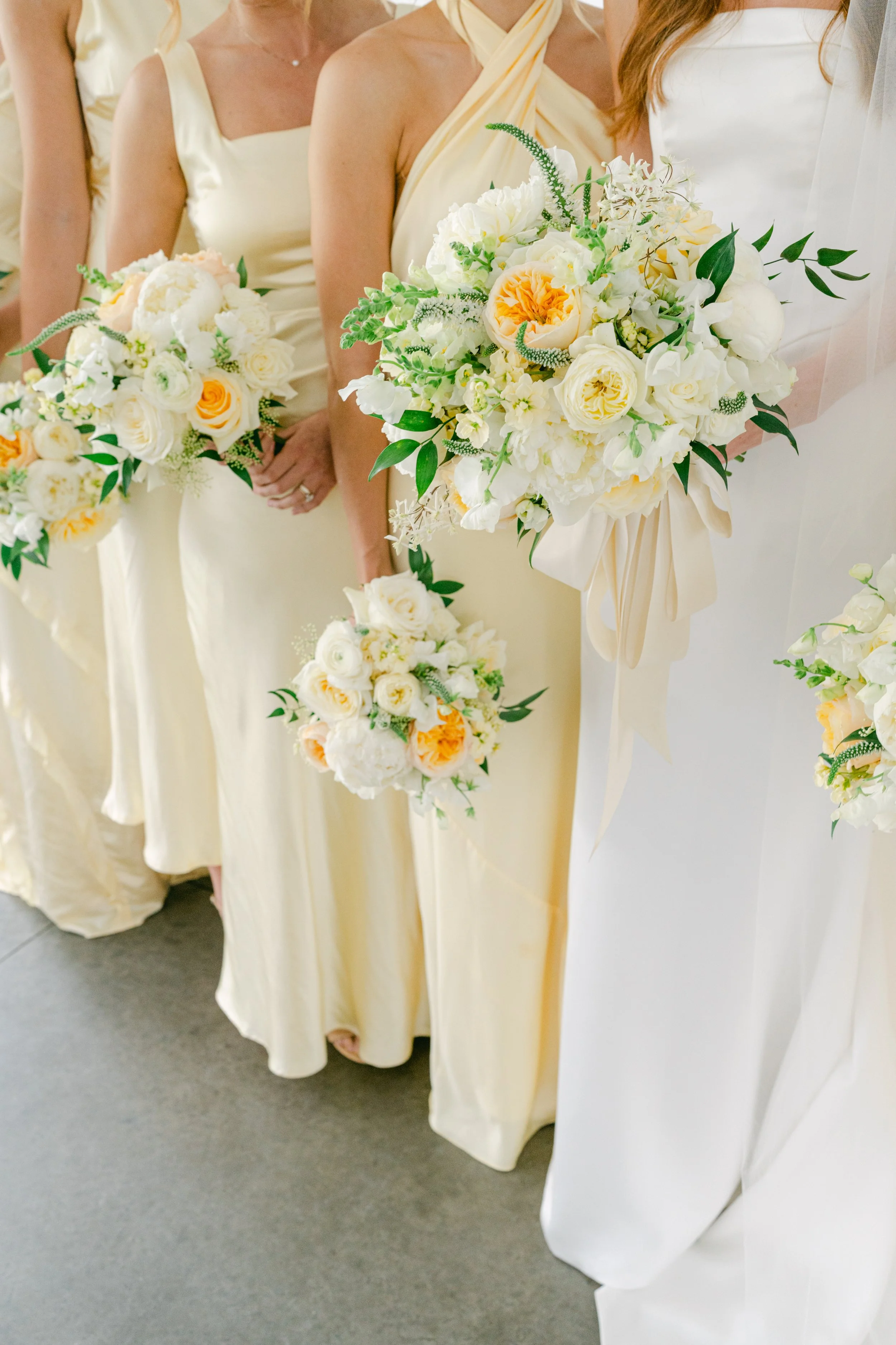 Group of women in yellow and white dresses holding bouquets at a wedding.