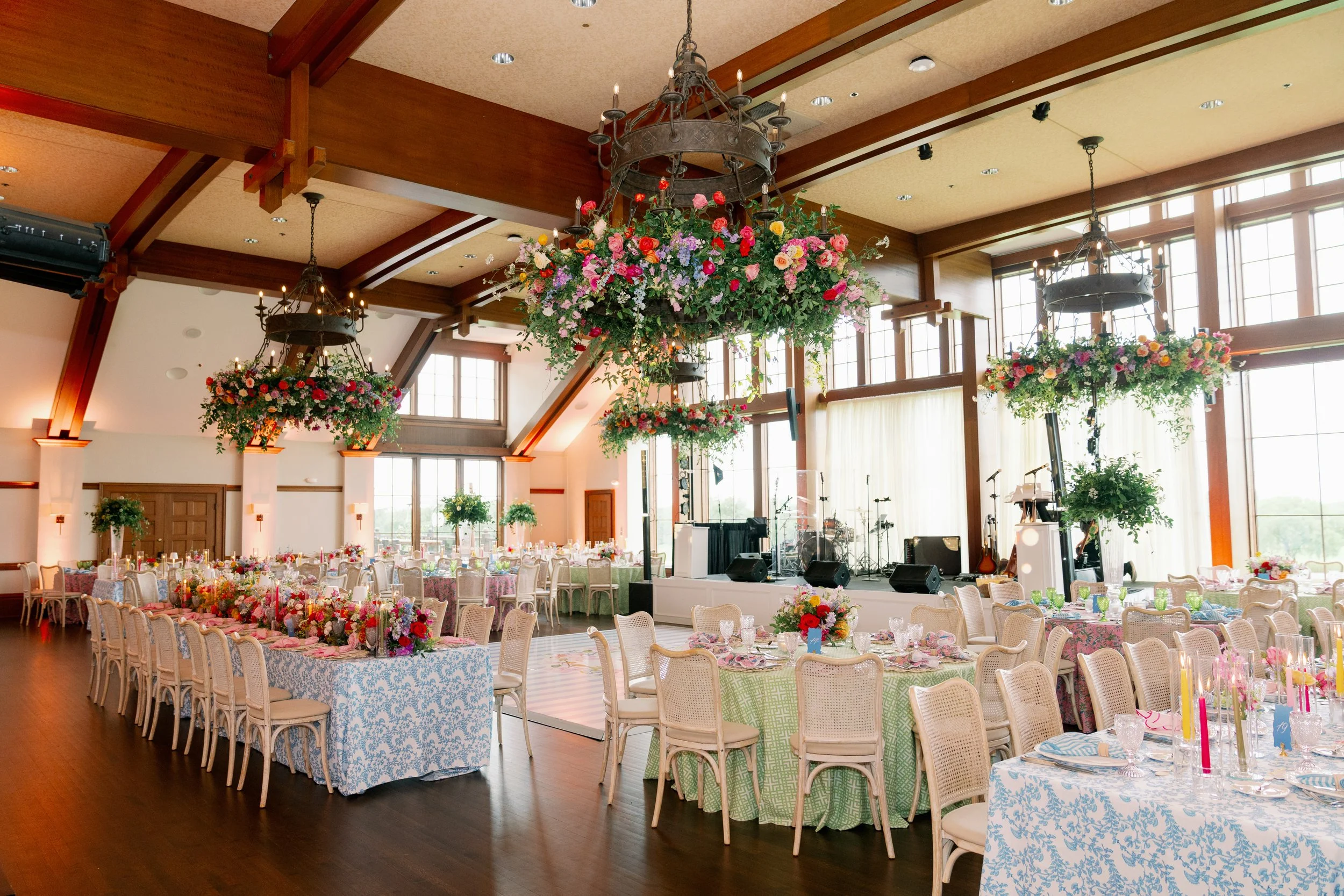 Banquet hall decorated with floral centerpieces, chandeliers, and tables set for a celebration or wedding reception.