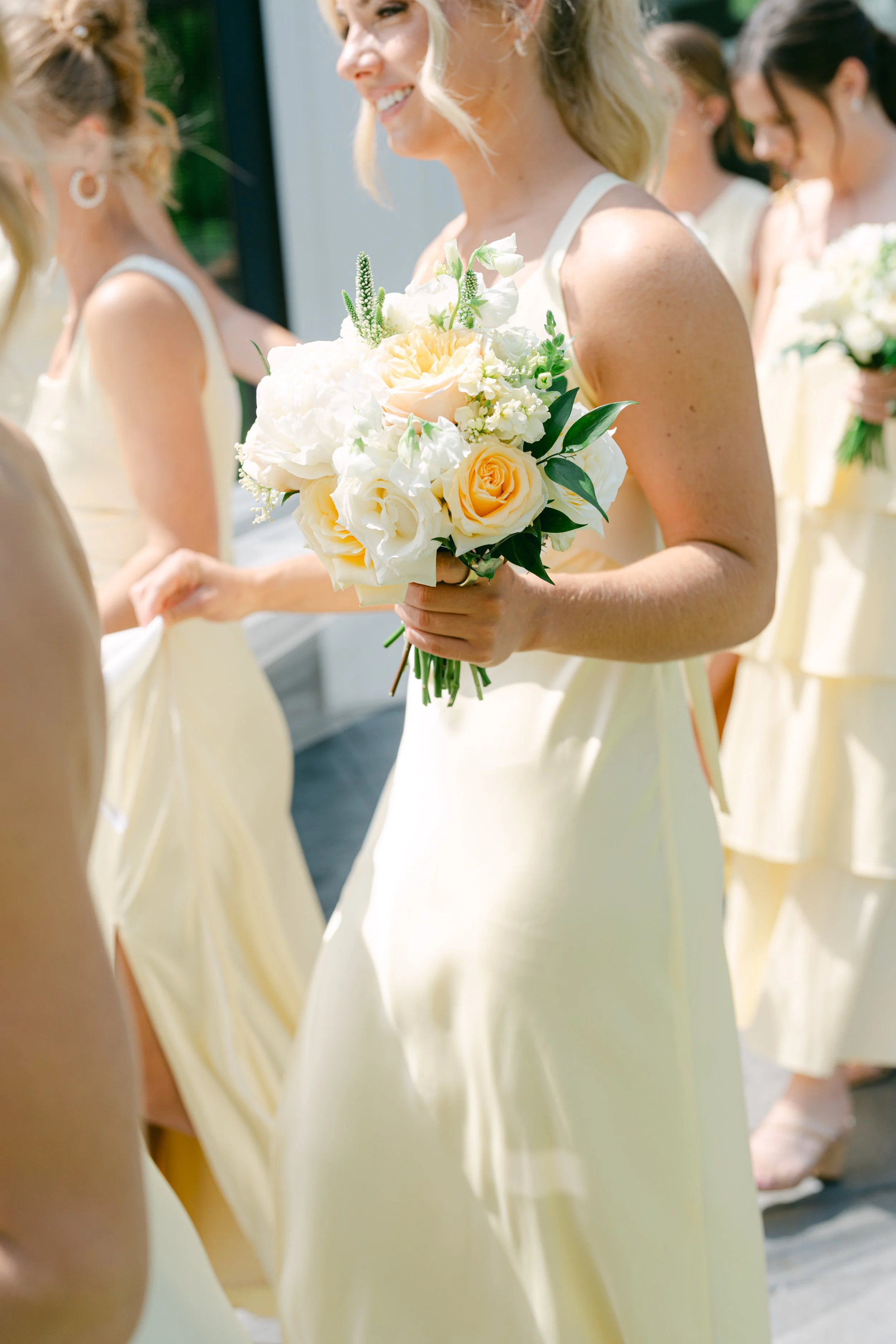 A bride holding a floral bouquet, surrounded by bridesmaids in matching cream-colored dresses during a wedding ceremony.