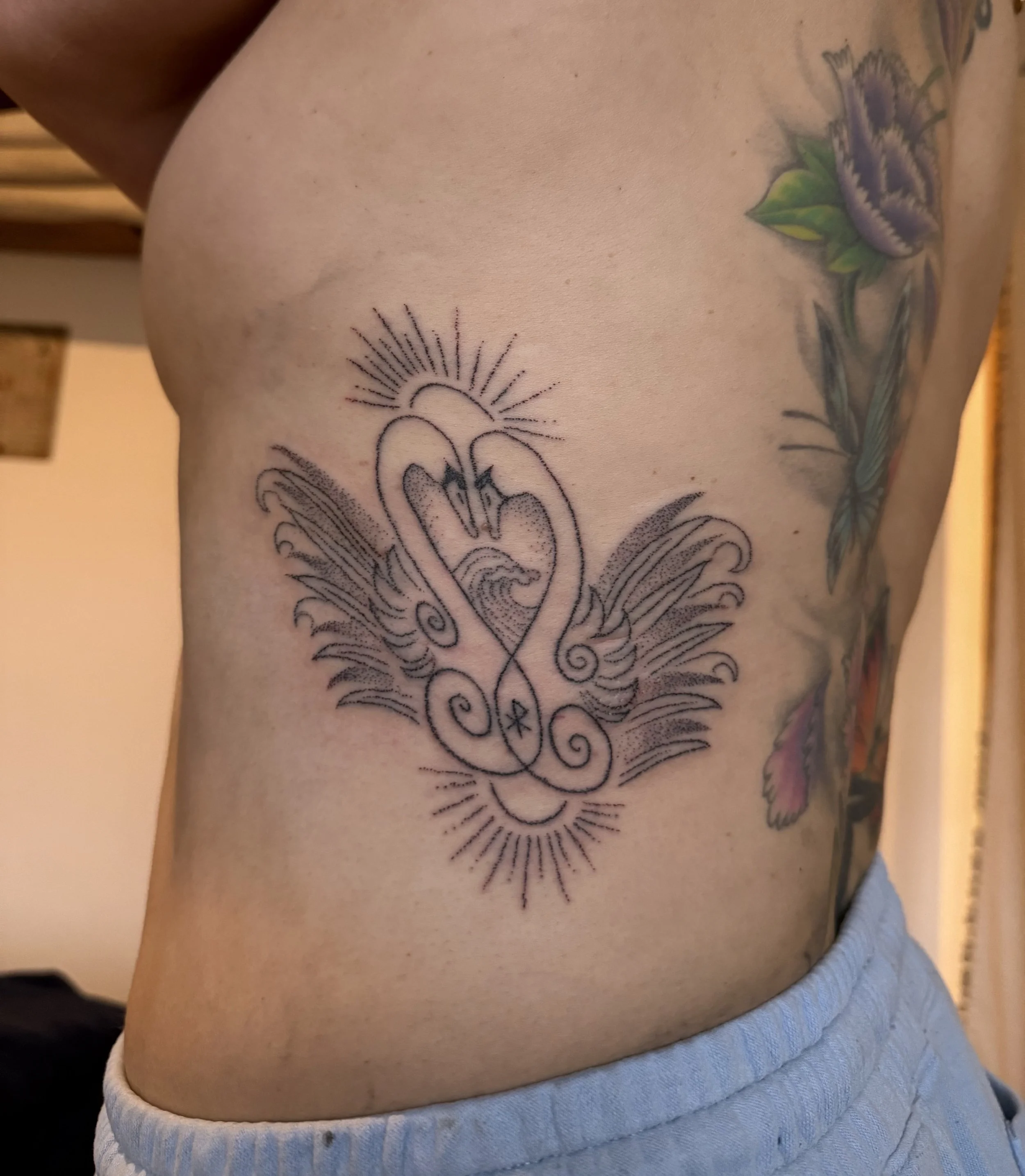 Tattoo of a stylized design with lines and curves, located on the person's side ribcage area, near the armpit and waist.