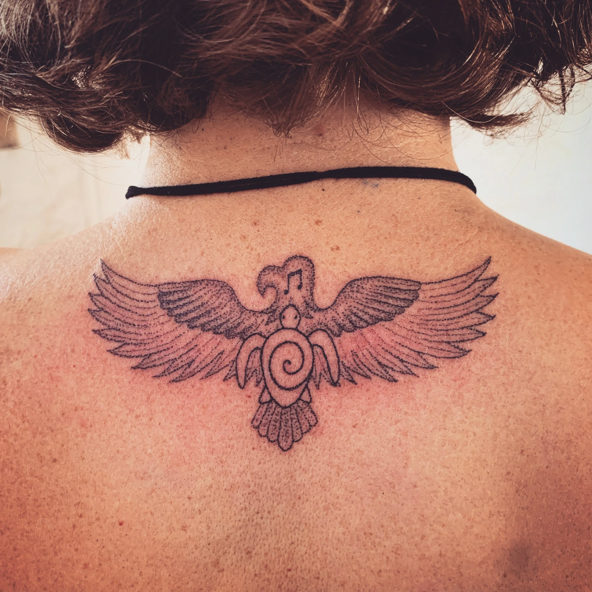 Back of a person's neck with a tattoo of the word 'love' surrounded by wings.