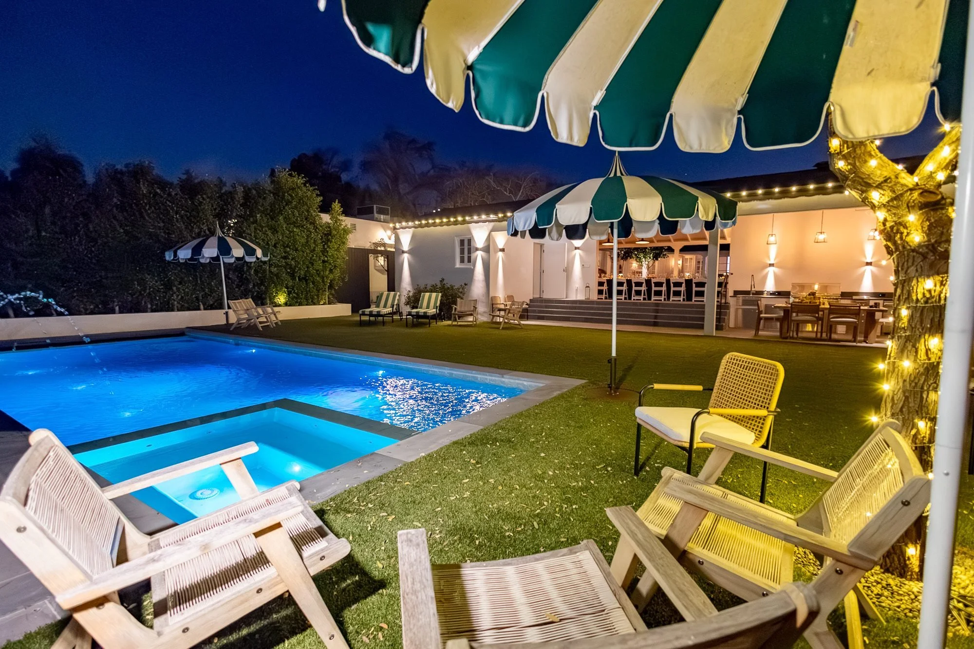 Pool illuminated at night beside a tree wrapped in fairy lights