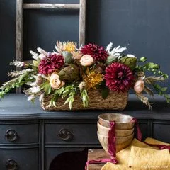 A floral arrangement with various flowers in a basket, placed on a dark table.