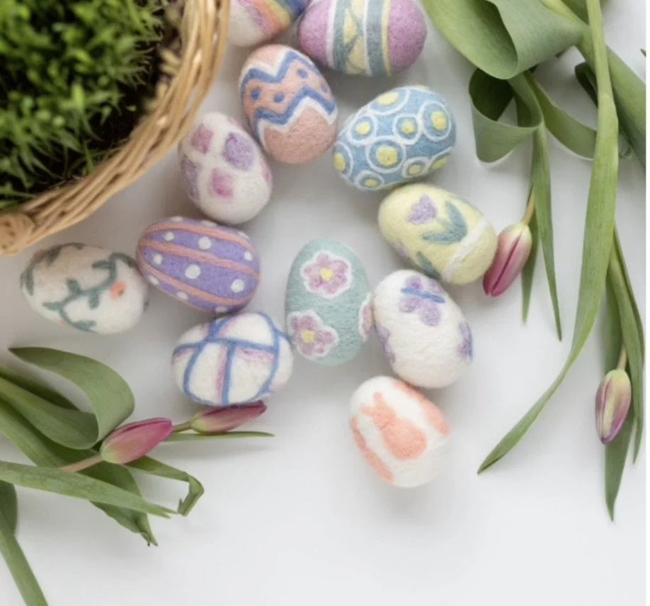 Decorative Easter eggs with pastel and floral patterns, surrounded by pink tulip buds and green leaves, on a white background.