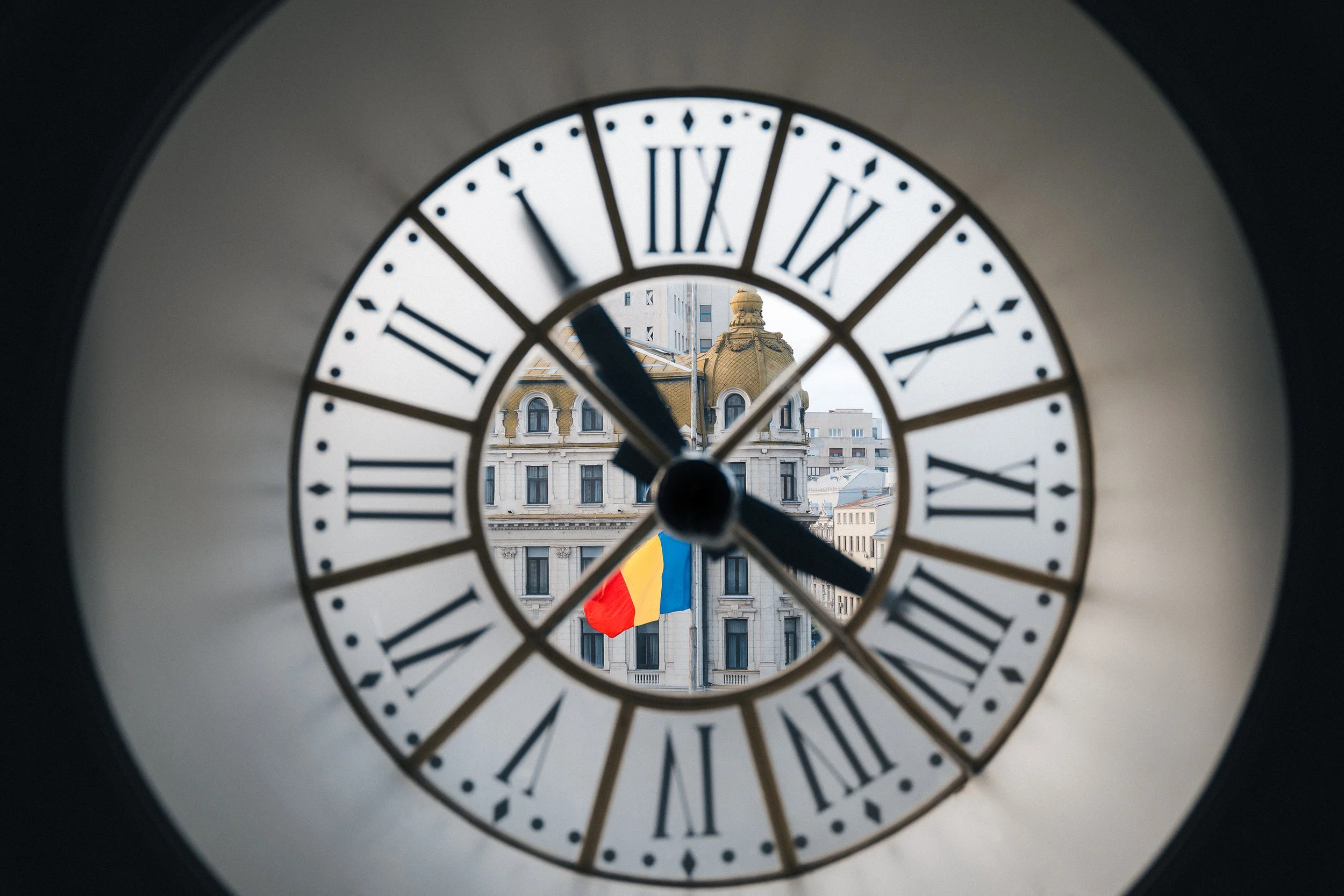 Clock face showing approximately 9:55, with a historic building and the Romanian flag visible through the clock window.