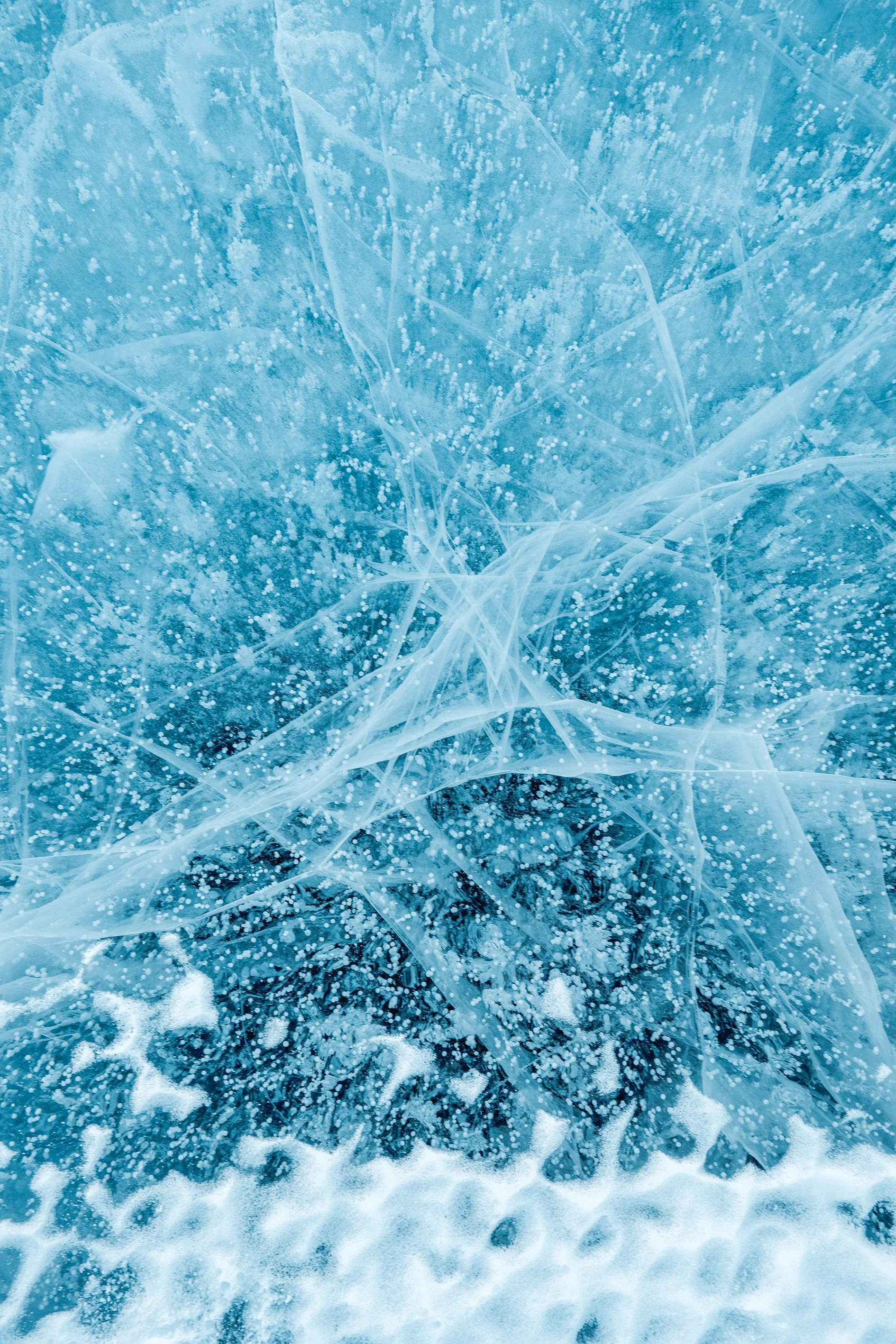 Close-up of cracked and shattered ice with frozen air bubbles and snow at the bottom.