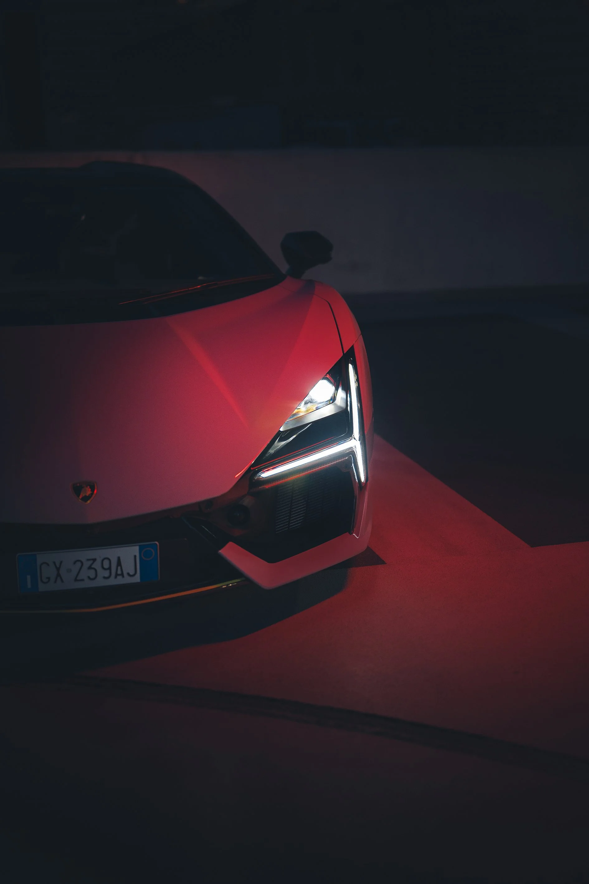 Close-up of a red luxury sports car with LED headlights and Italian license plate, in a dark setting.