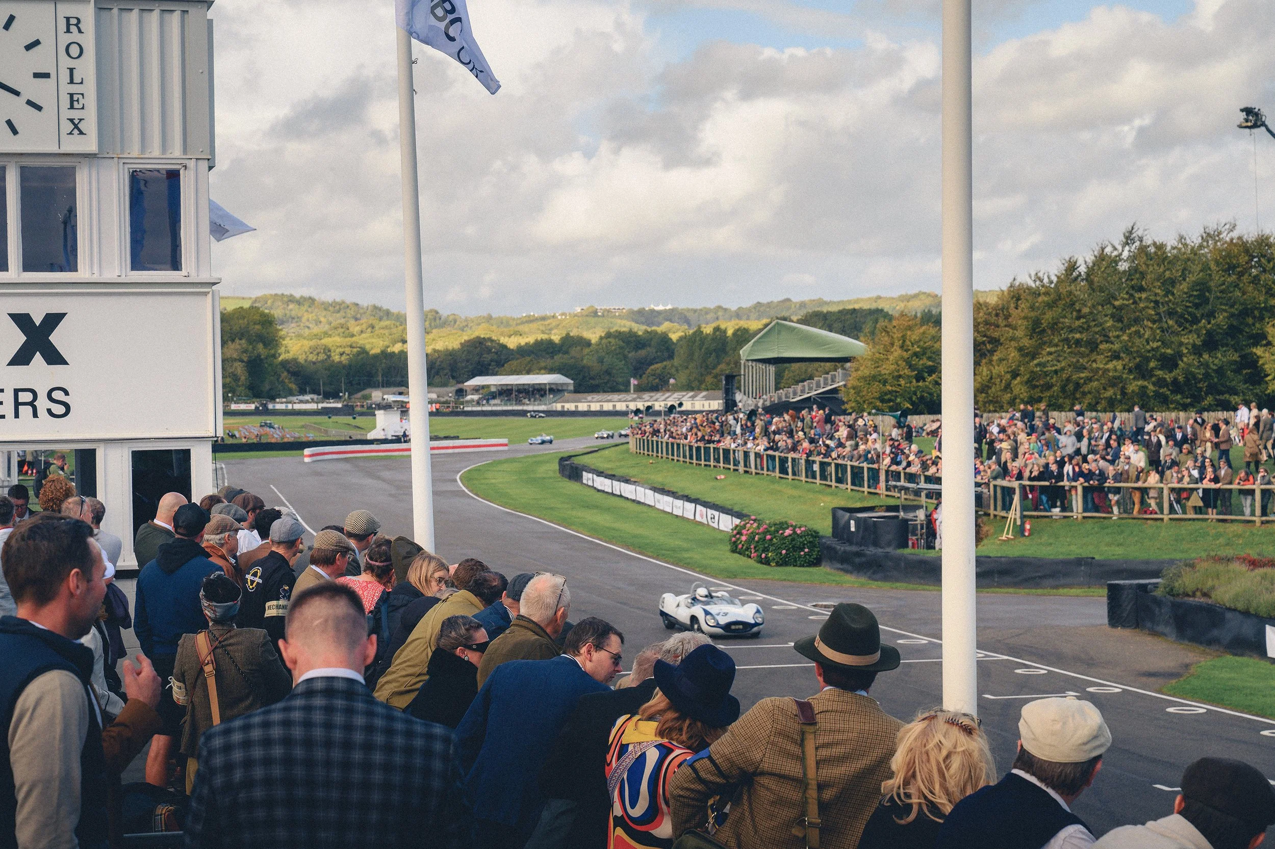 Crowd watching a race at a historic racing event with a small vintage race car on the track