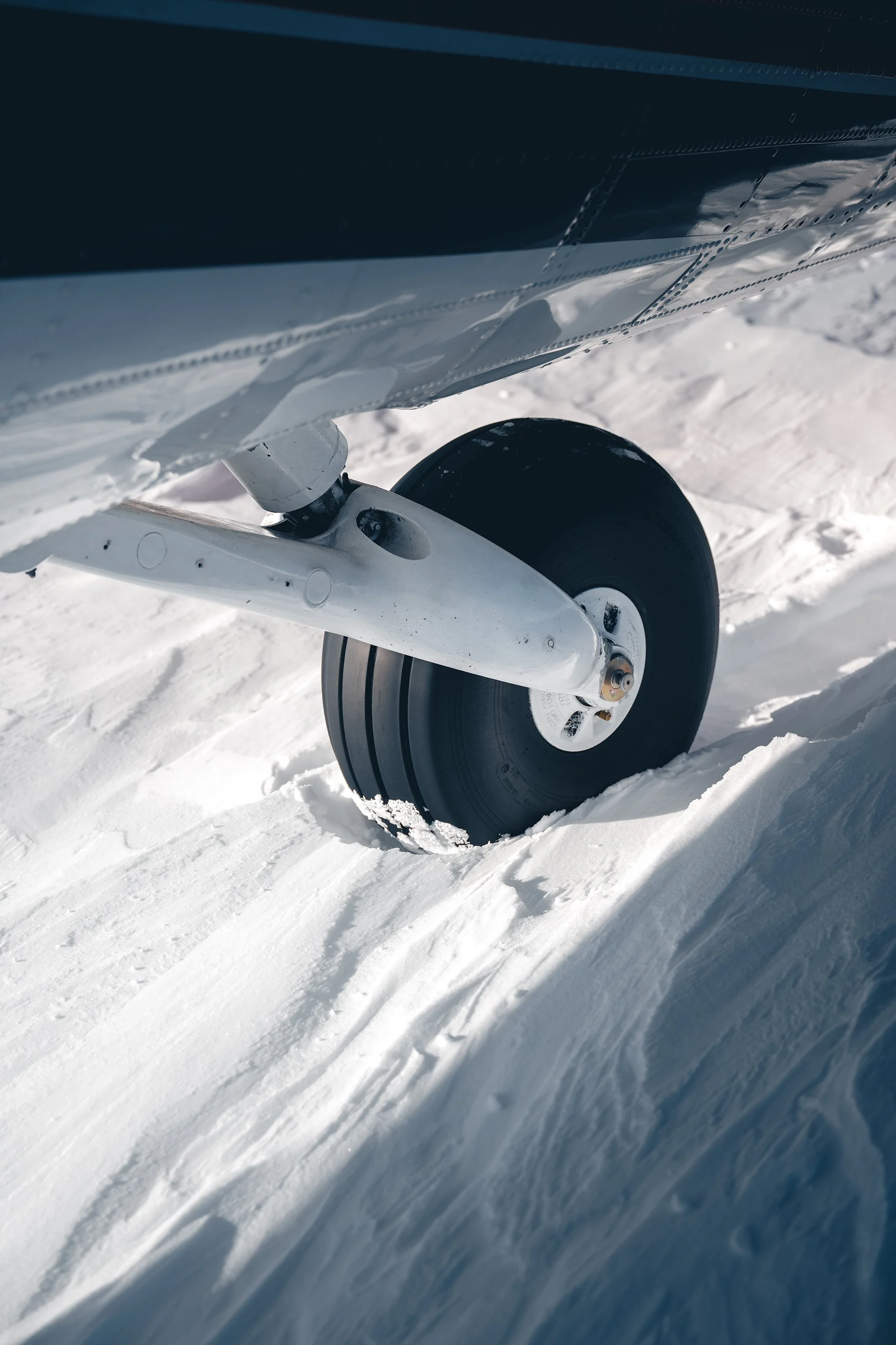 Close-up of airplane landing gear wheel on snow-covered ground.