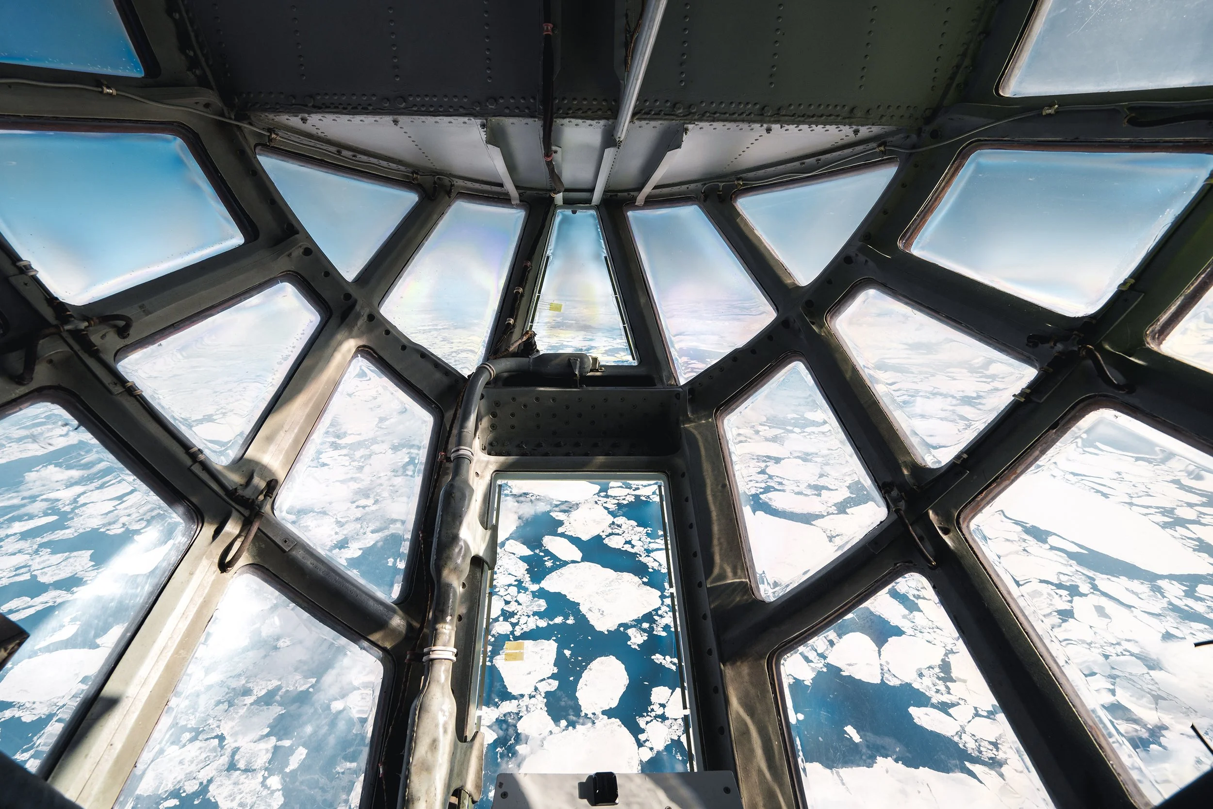 View from inside the cockpit of an aircraft flying above Arctic ice and water.