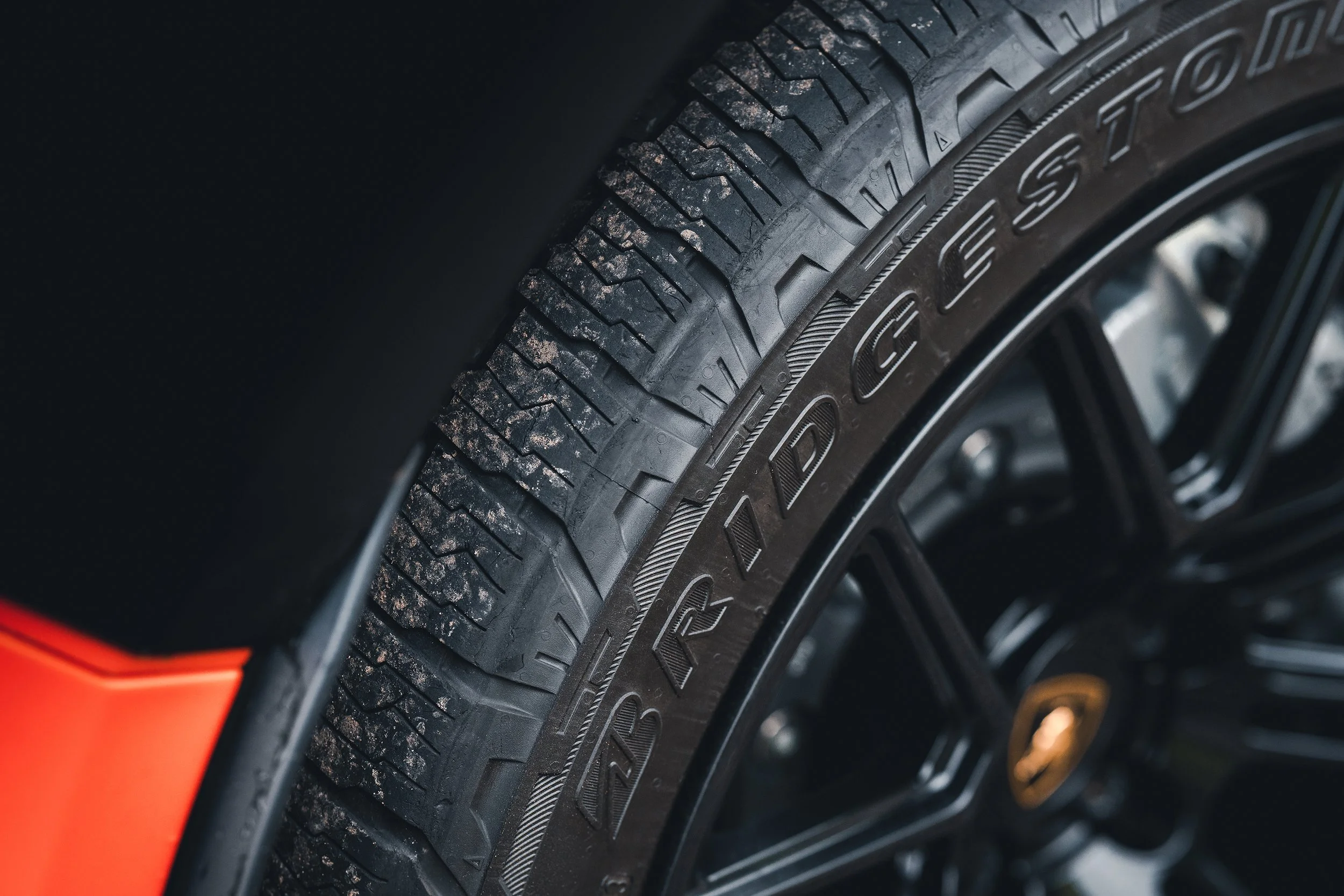 Close-up of a car tire with tread patterns and the brand name 'TRI GEAR' visible on the sidewall, mounted on a black alloy wheel with a gold center cap.