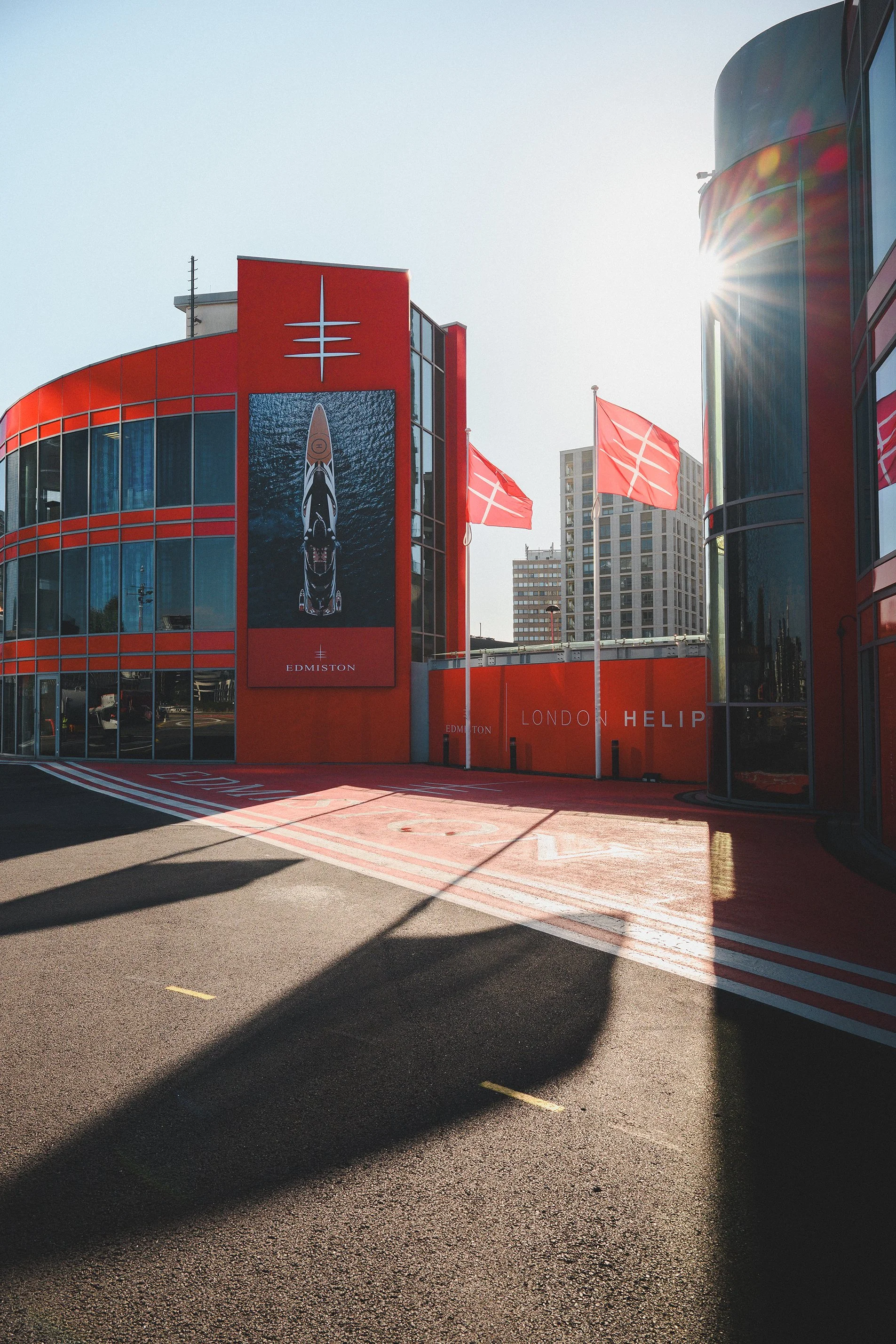 Photo of the London Helipad at London Heathrow Airport with red buildings, flags, and shadows on the ground