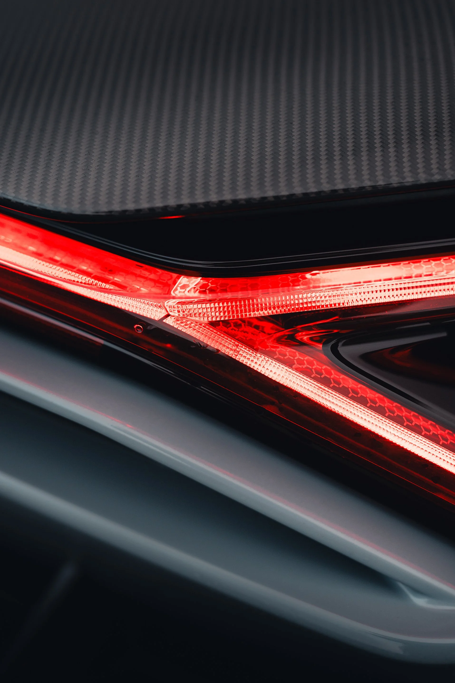 Close-up of a car's tail light with a black carbon fiber surface on top.