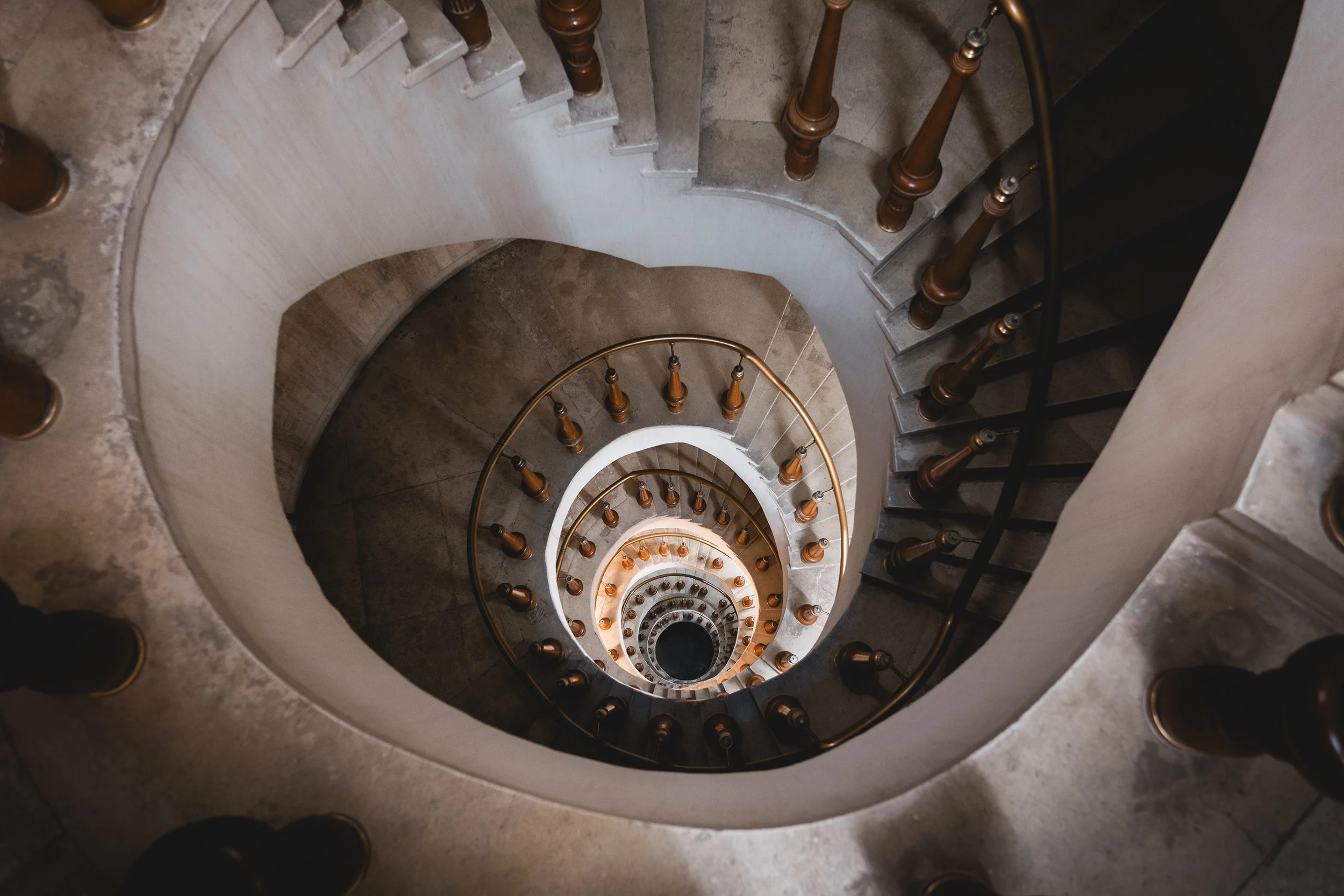 View looking down a spiral staircase with wooden railings and steps, with the staircase decreasing in size as it spirals downward.