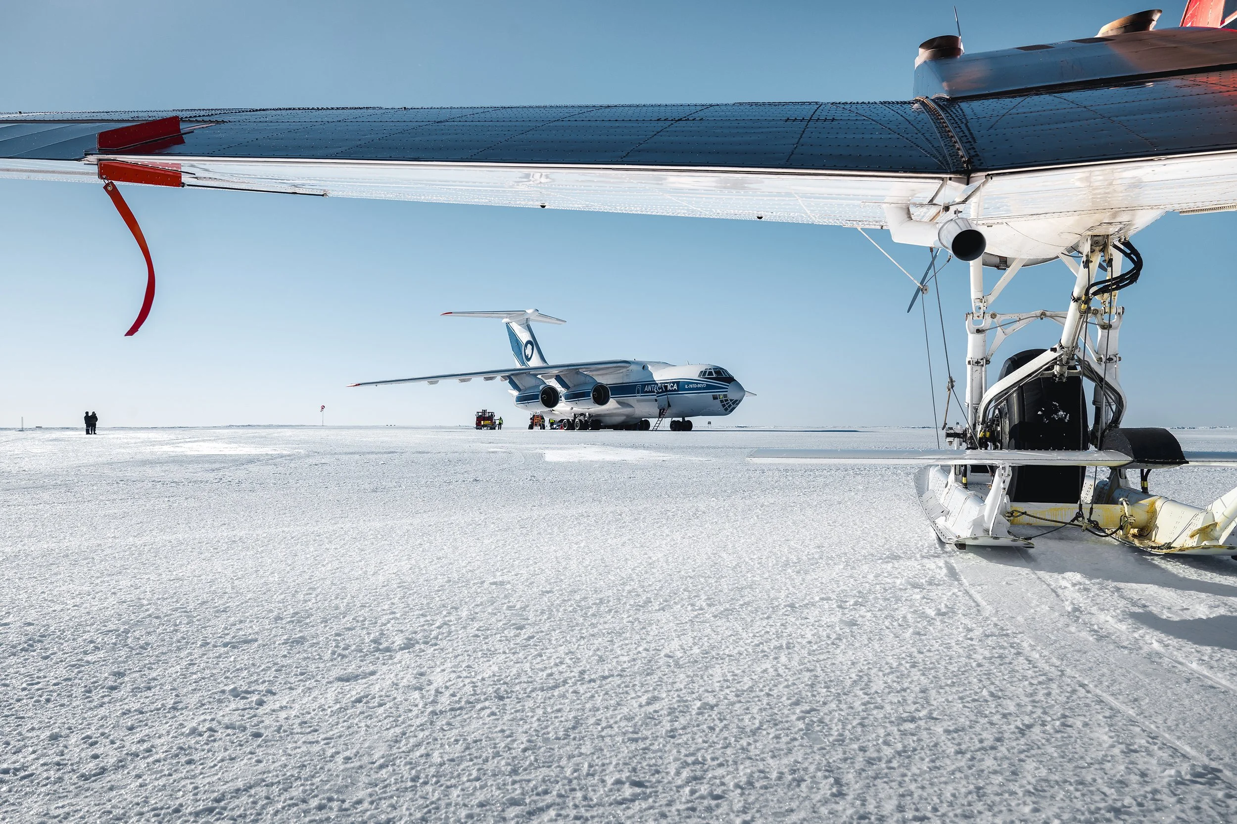 An aircraft and a snowmobile on a snowy, flat landscape with a clear blue sky.