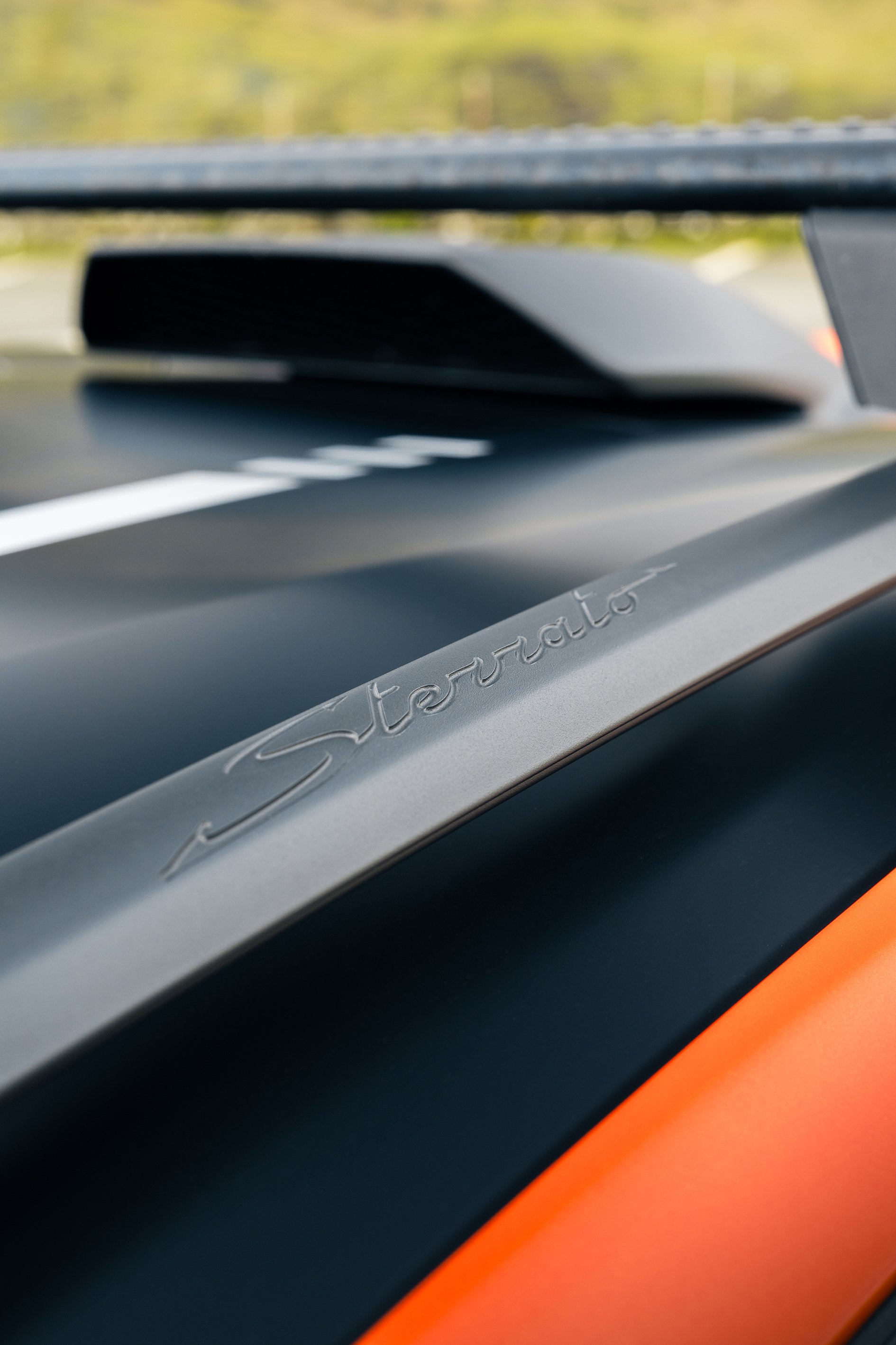 Close-up of a Porsche Sportair badge on the hood of a sports car, with the car's orange and black paint visible.