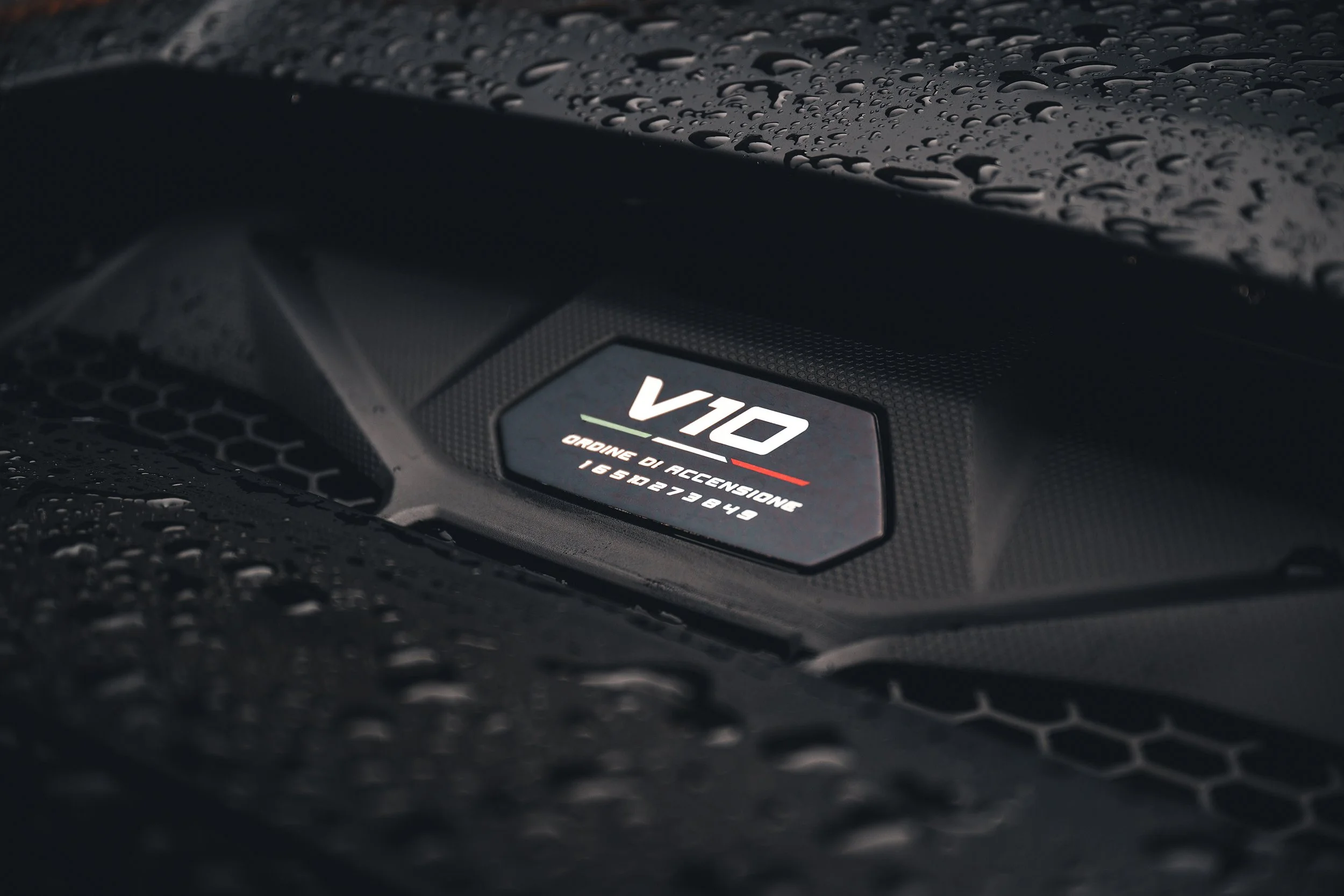 Close-up of a Lamborghini V10 engine badge on a wet black car hood.