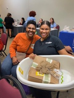 A loving mother stands proudly beside her daughter during the Fort Bend County Community Baby Shower, offering encouragement and support as they receive baby items together. A beautiful moment of family unity and generational strength.