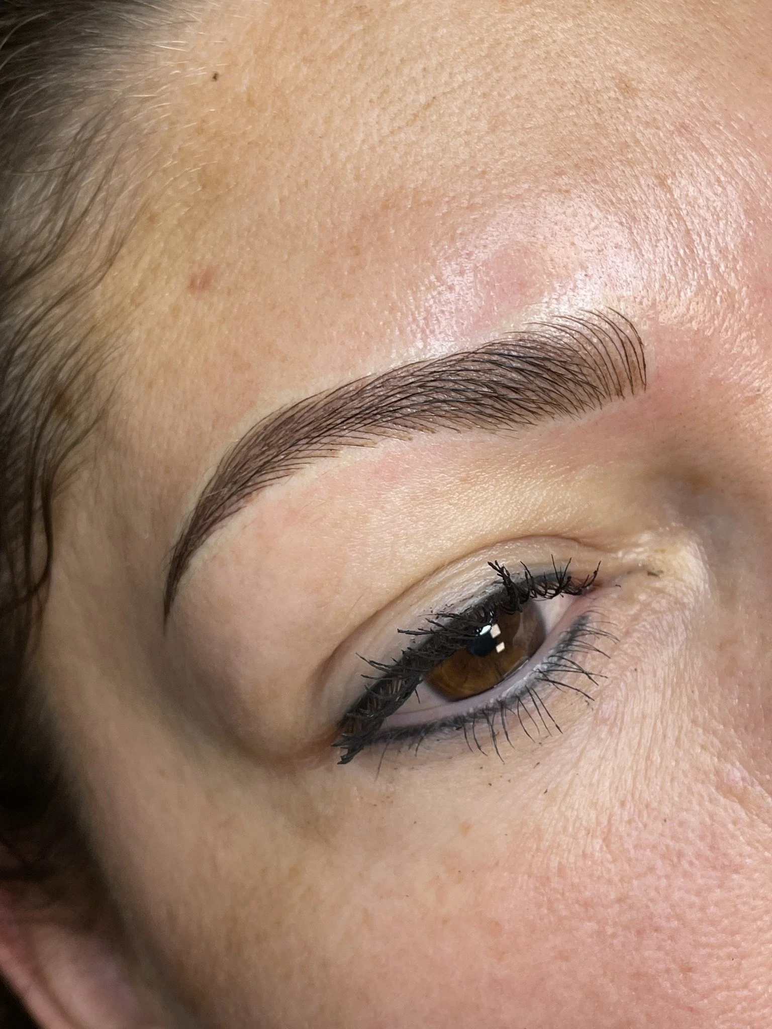 Close-up of a person's eye with well-groomed eyelashes and eyebrow, showing skin texture around the eye.