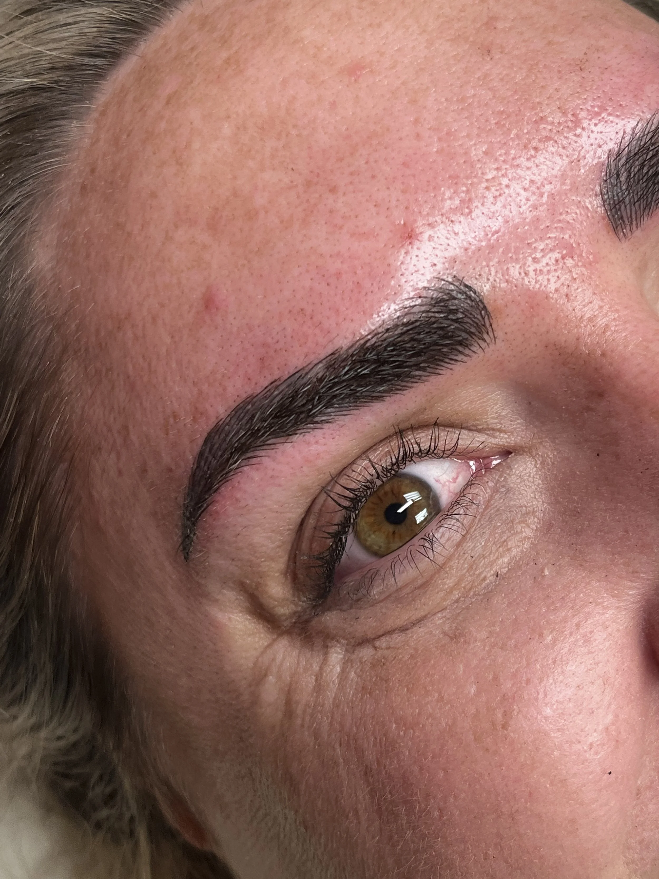 Close-up of a person's forehead and eye, showing clear skin and natural brown eye with long eyelashes.