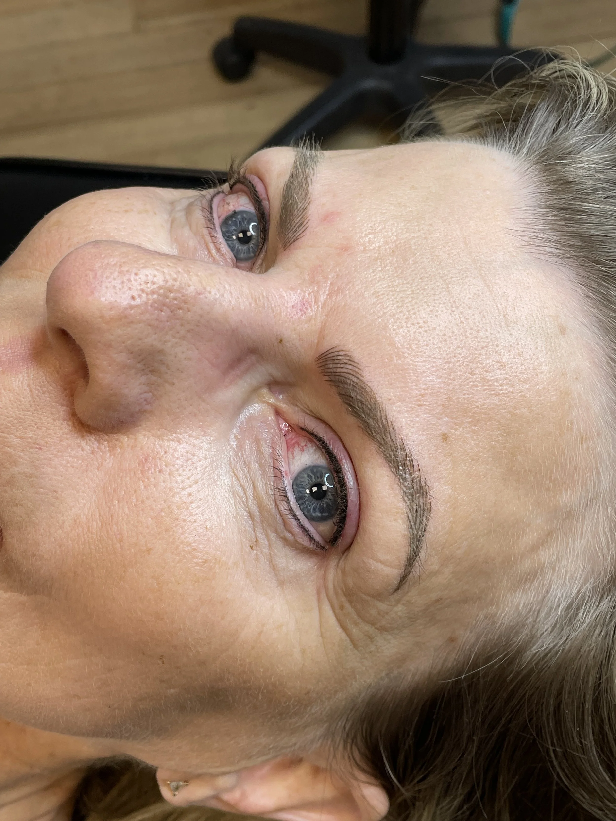 A woman lying on her back with her head tilted to the side, showing her face and blue eye.