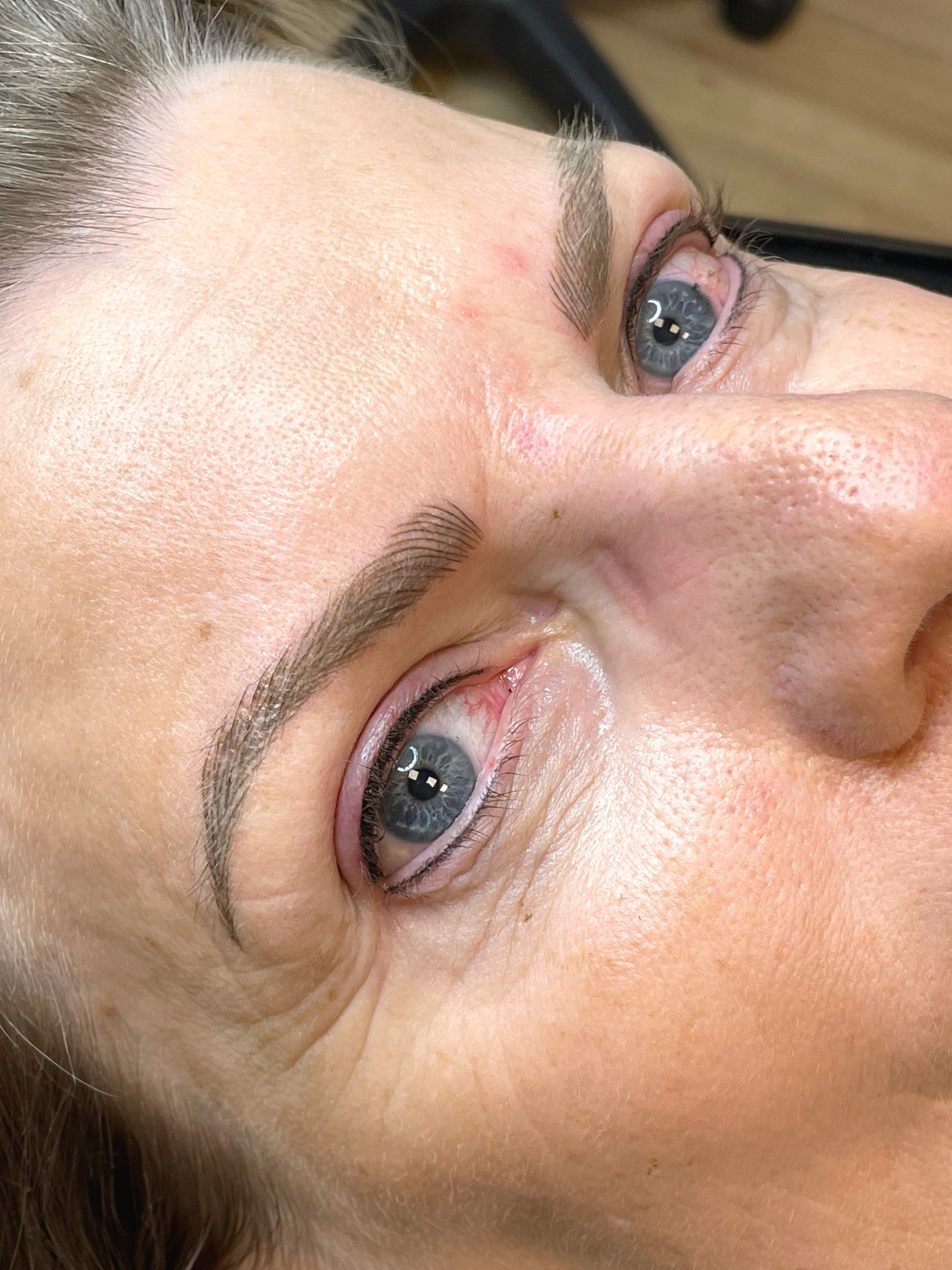 Close-up of a person's face lying down, showing their eye, eyebrow, and skin texture.