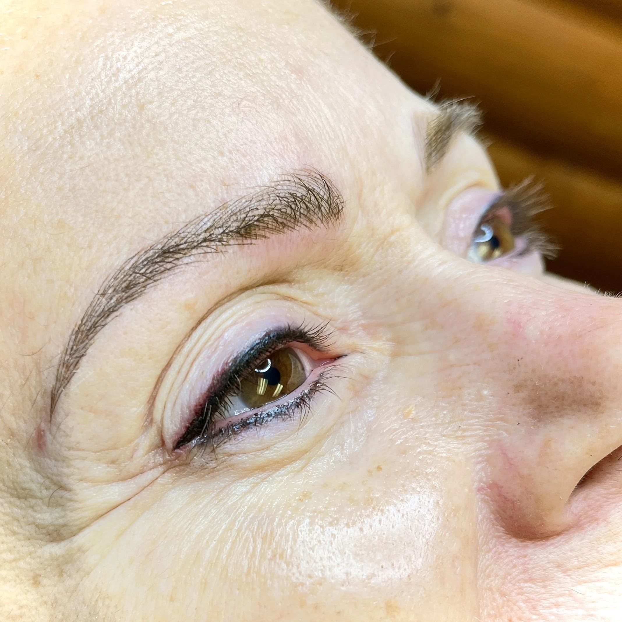 Close-up of a person's eyebrow, eye, and surrounding skin with a small blemish and some skin texture visible.