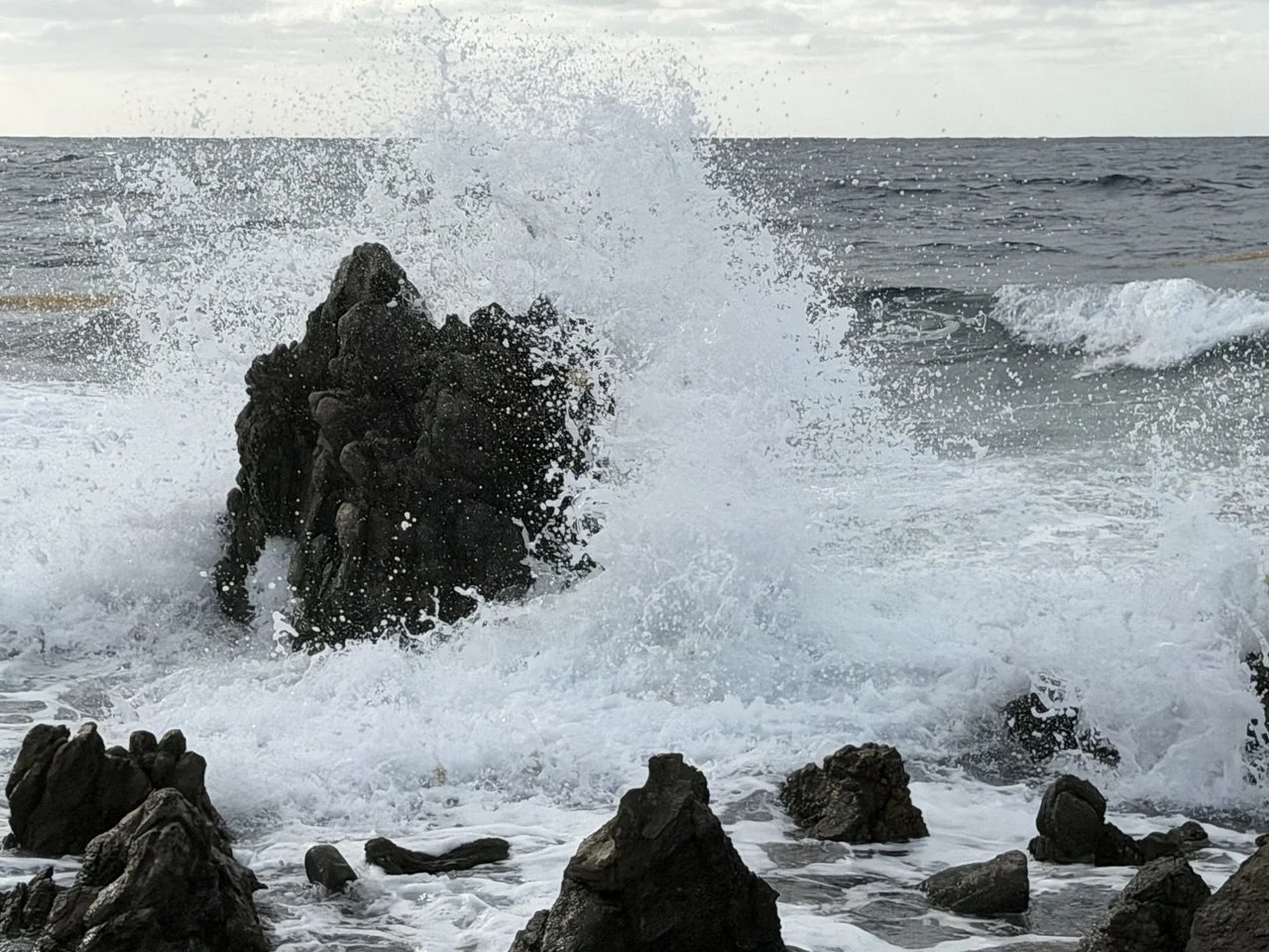 Ocean waves crashing against dark rocks on a cloudy day.