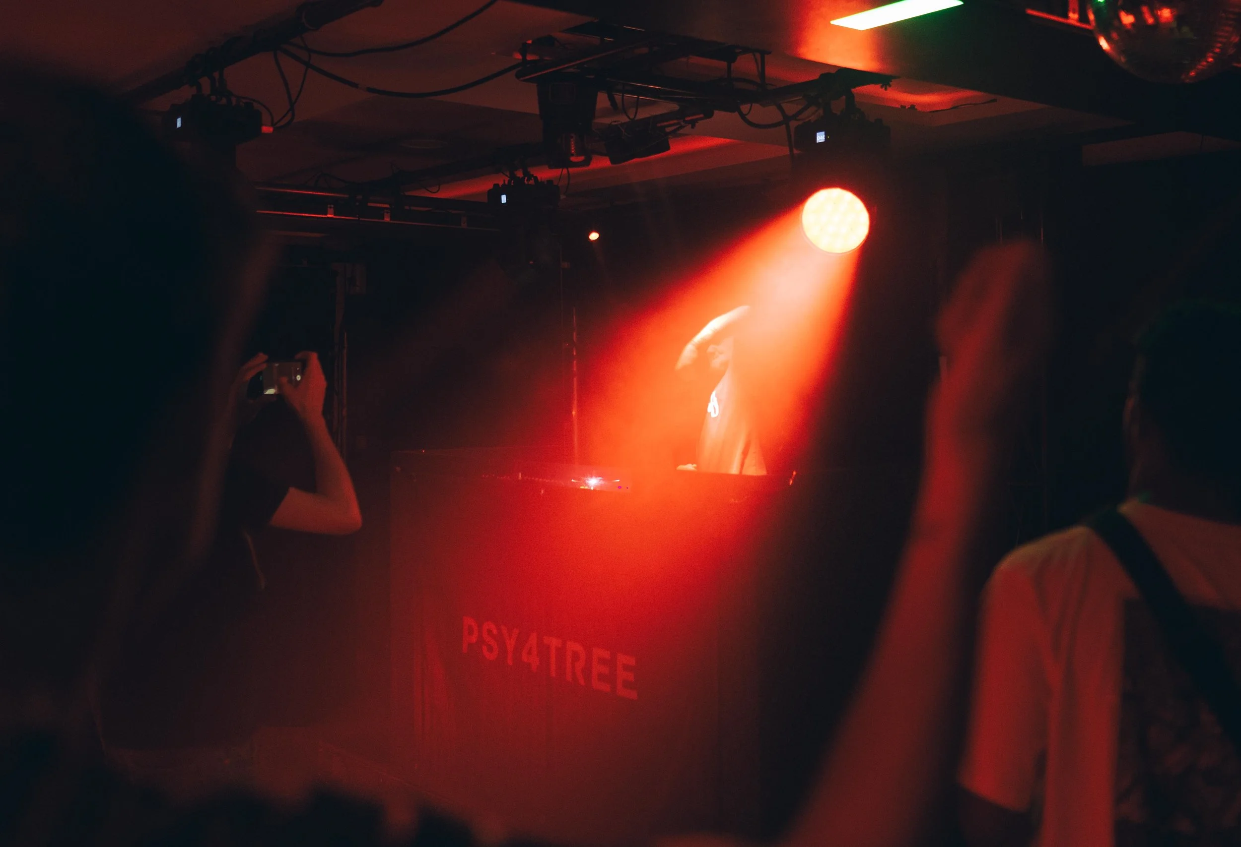 Participants dans une salle sombre avec éclairage rouge, certains prennent des photos, une personne debout est partiellement visible, derrière un panneau avec le texte 'PSY4TREE'.