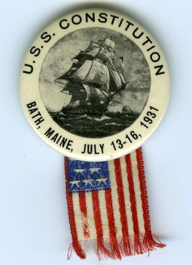 A pin with a depiction of the U.S.S. Constitution, and commemorating its 1931 visit to Bath. A small U.S. flag is attached. BHS2010.17.10