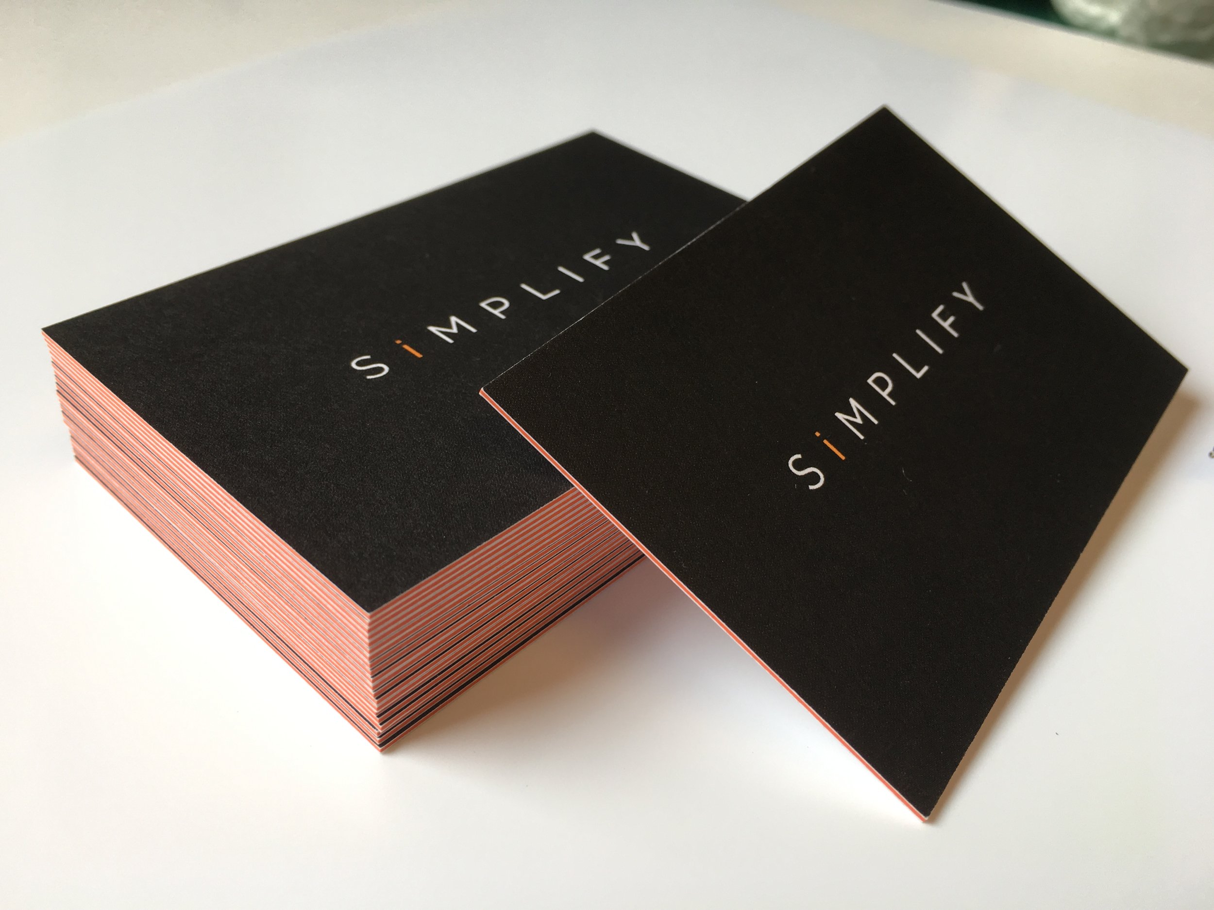 Stack of Resilient Cognitive Solutions (RCS) black business cards with orange and white text that says 'SIMPLIFY', placed on a white surface.