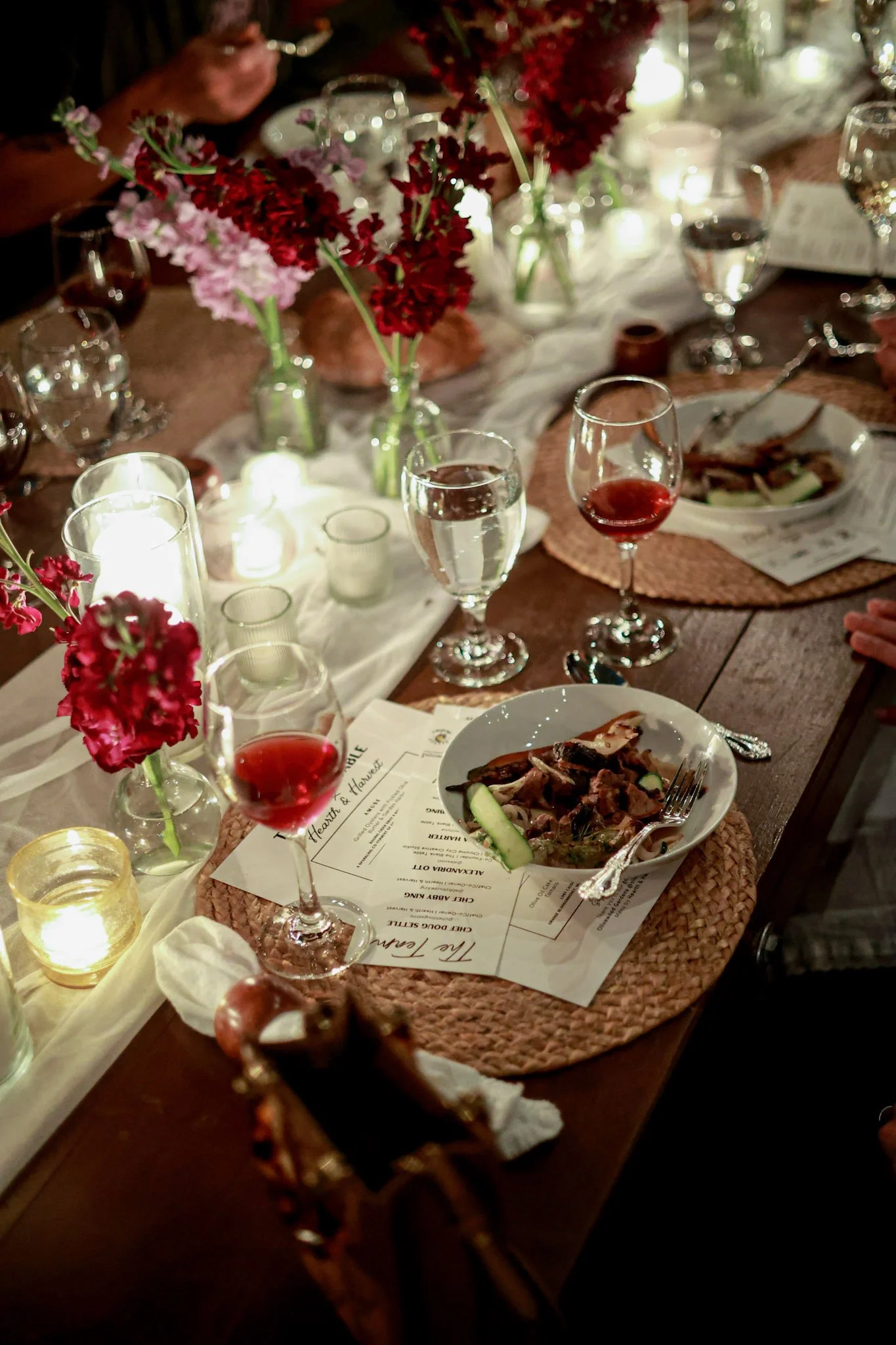 Community dining scene with shared plates, candles, and seasonal flowers at a Hearth & Harvest live-fire feast in San Diego, celebrating connection through food.