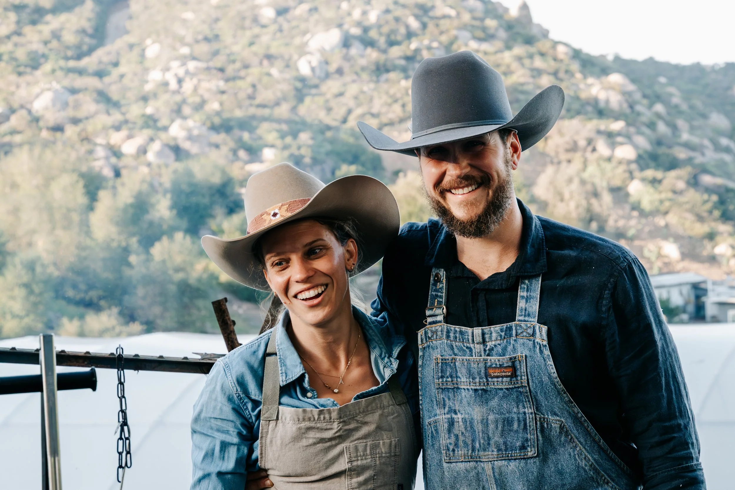 Hearth & Harvest chefs in cowboy hats and aprons at an open-air farm setting, representing a live-fire farm-to-table dinner at Sage Hill Ranch Gardens
