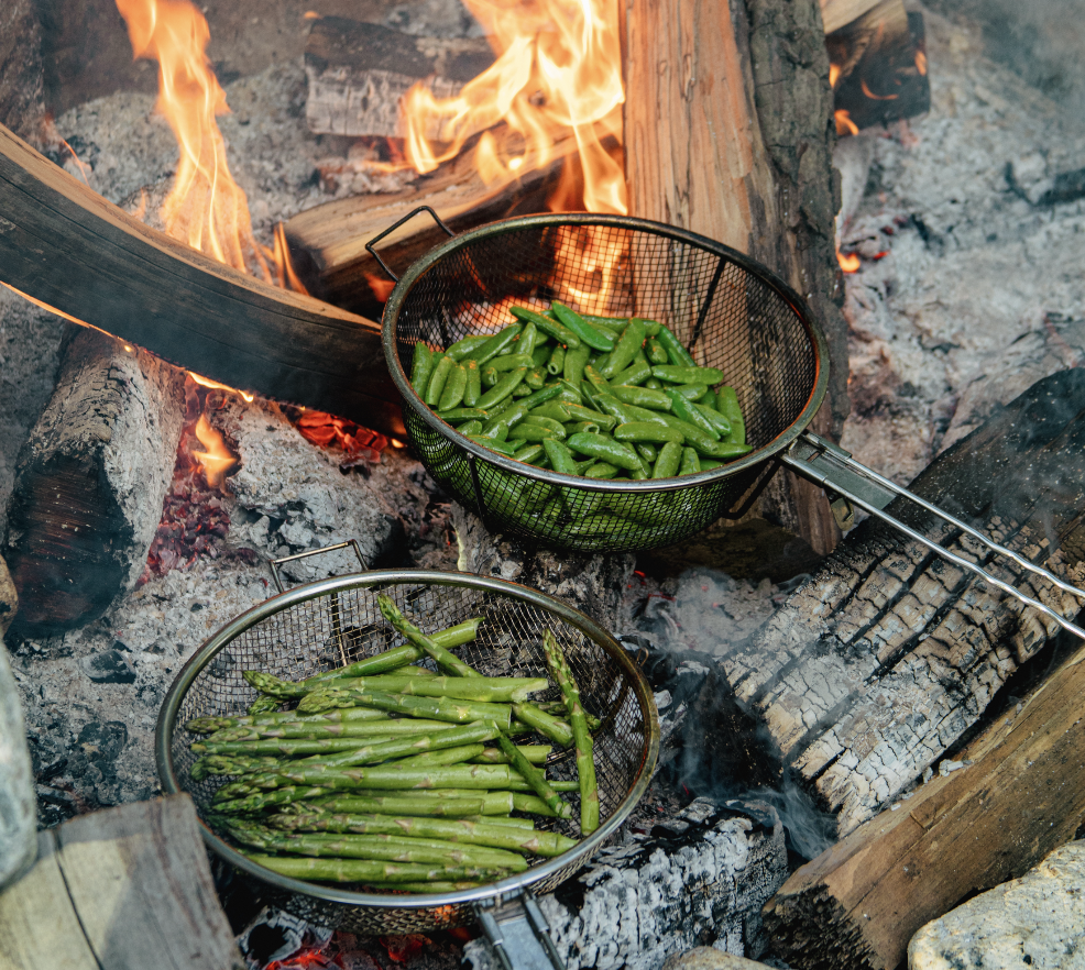 Asparagus and snap peas roasting over an open fire, showcasing Hearth & Harvest’s storytelling through ingredient-driven, live-fire cooking.