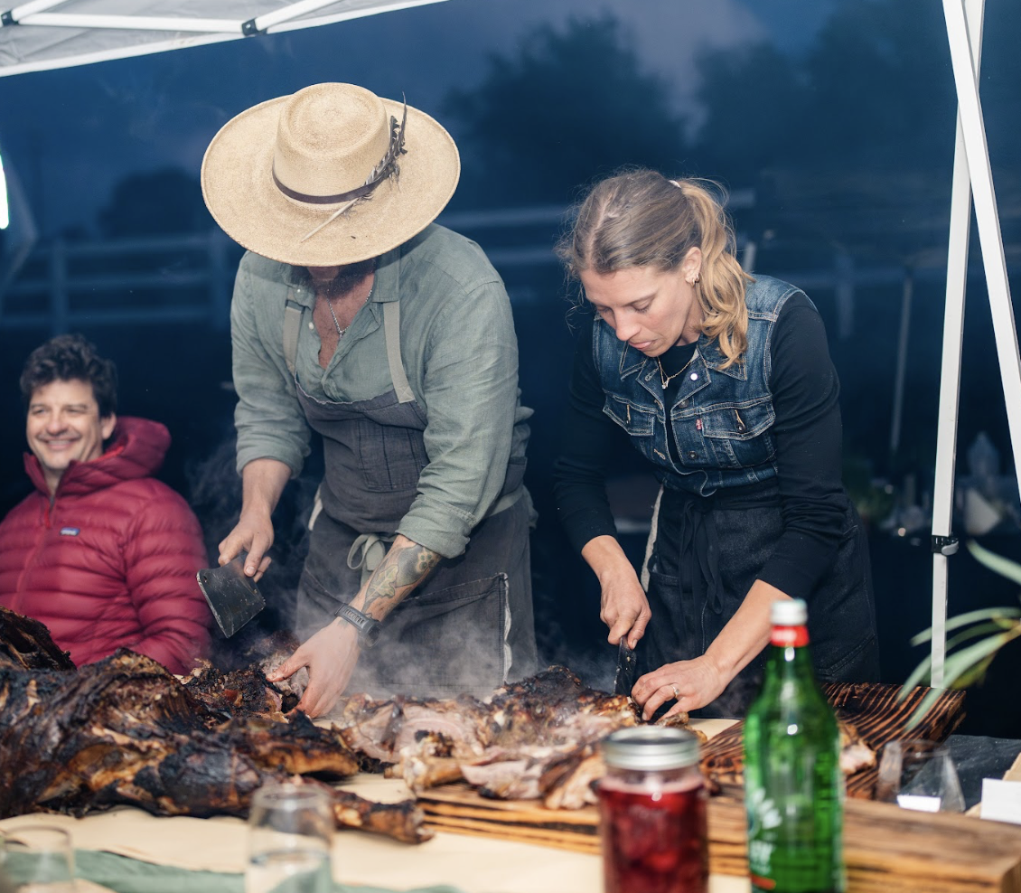 Chefs carving and preparing fire-roasted meat at a Hearth & Harvest live-fire catering event in Southern California, showcasing hands-on craftsmanship and experiential dining.