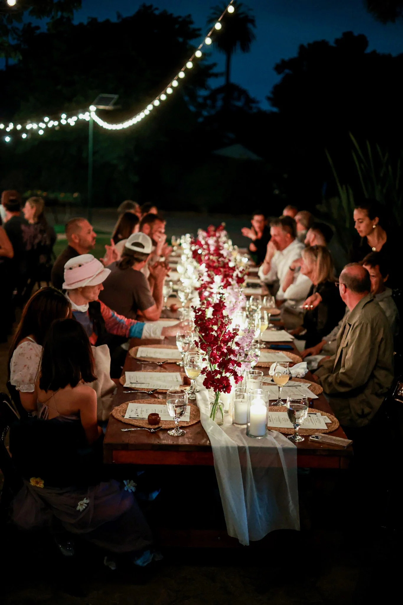 Outdoor farm-to-table dinner in Oceanside, CA featuring a long communal table with candlelight, seasonal flowers, and guests enjoying a Hearth & Harvest live-fire catered event in San Diego.