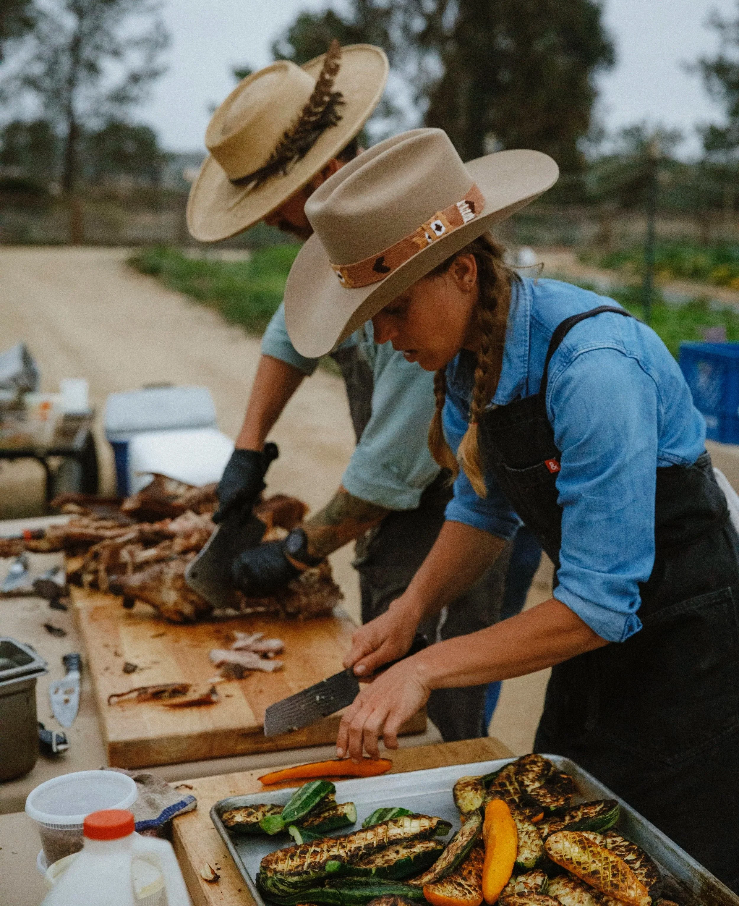 Hearth & Harvest chefs preparing grilled seasonal vegetables and carving meat at an outdoor live-fire catering event in Southern California.