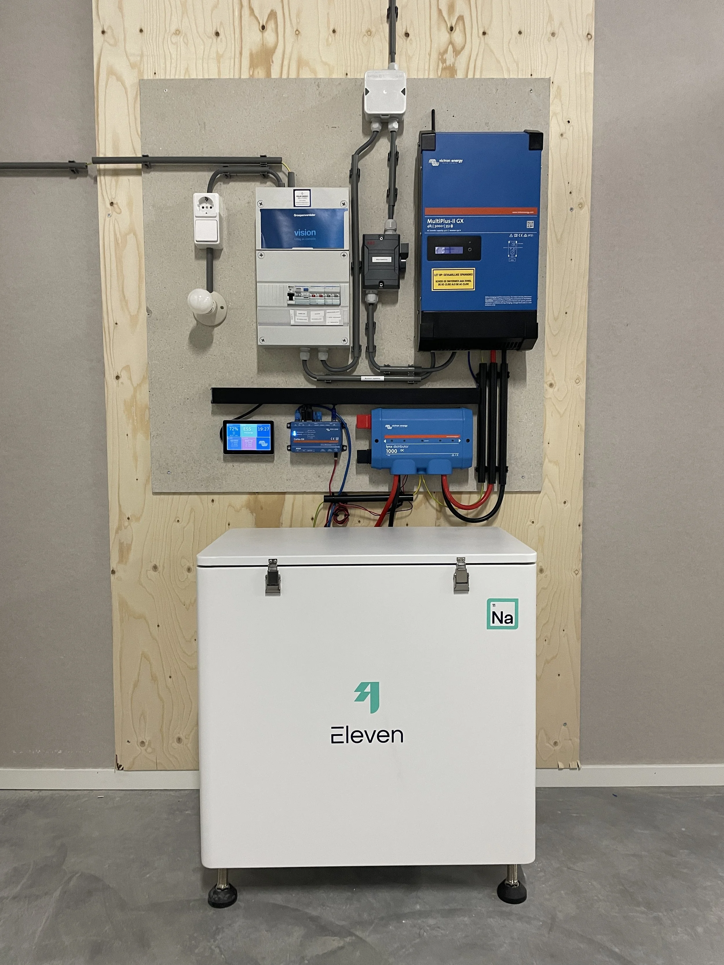 Een foto van een elektrische energietekken en configuratie, inclusief een omvormer, oplaadpunten en batterijen, geplaatst tegen een houten wand en gemonteerd op de muur en vloer.