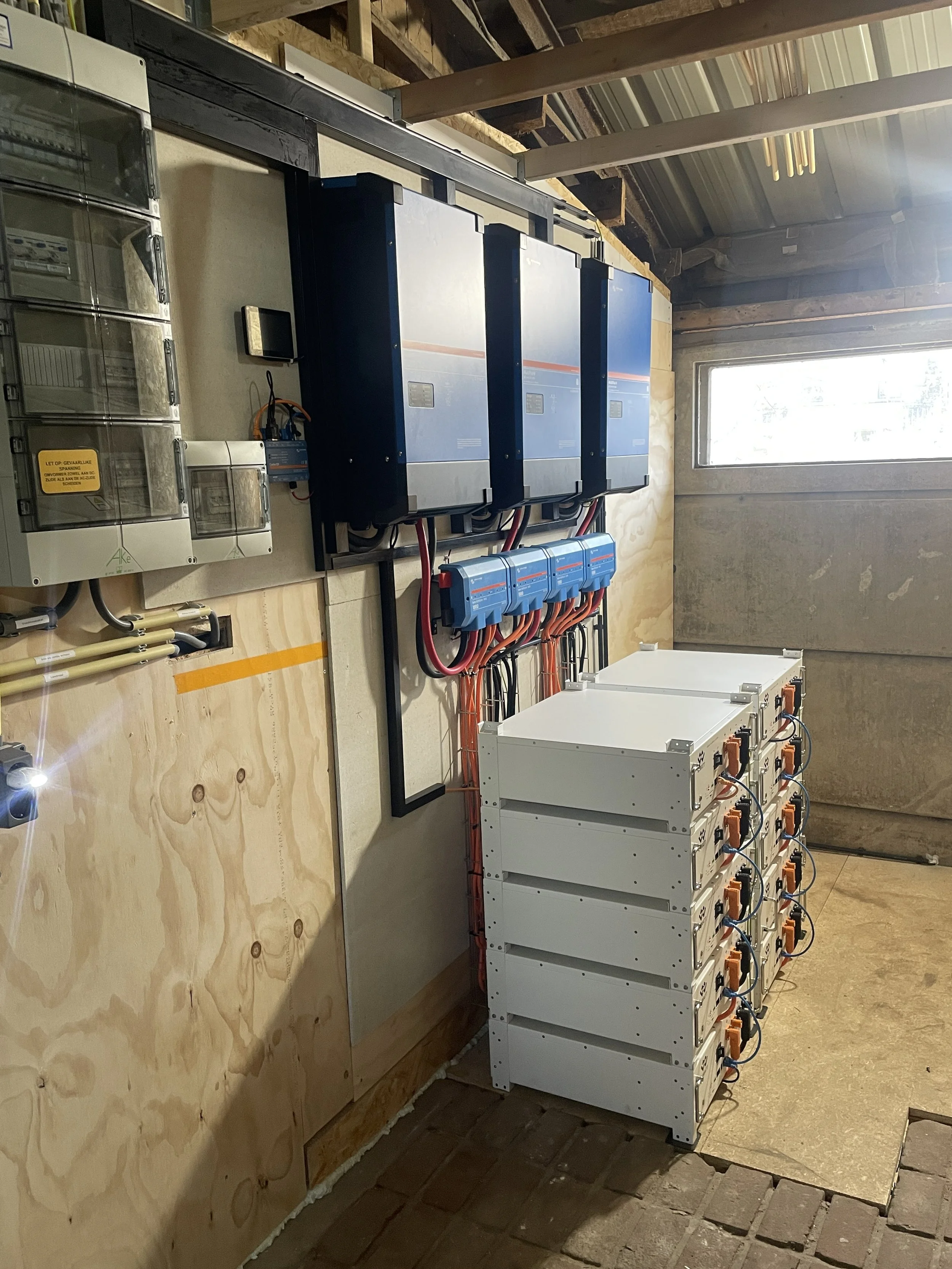 Elektrisch opstellingen met control panels, omvormers en batterijen in een technische ruimte.