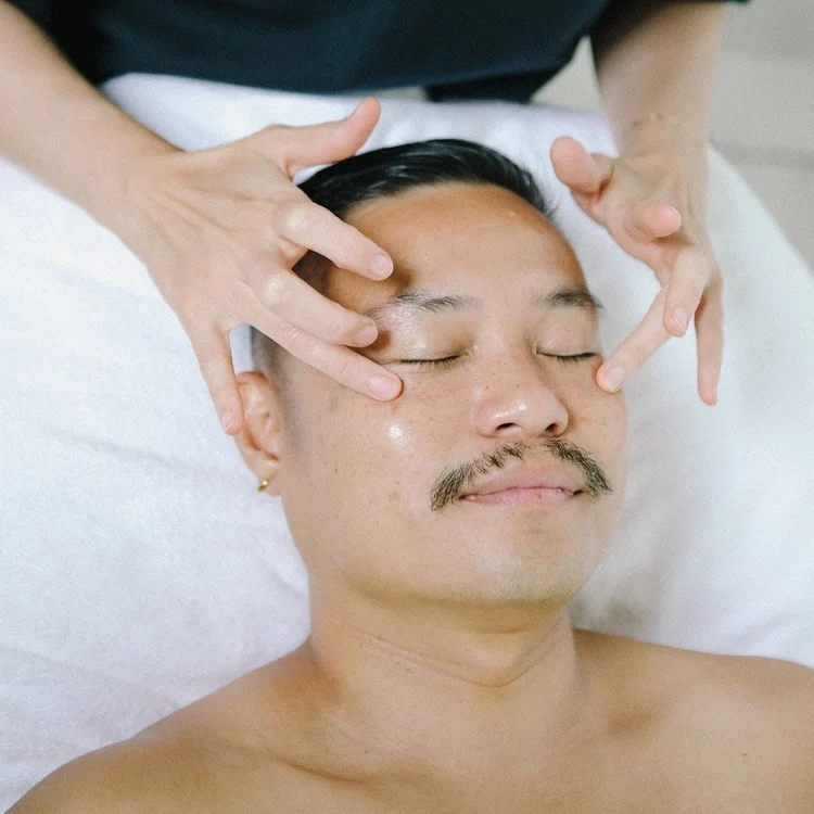 Person receiving a facial massage with closed eyes, lying on a treatment table.