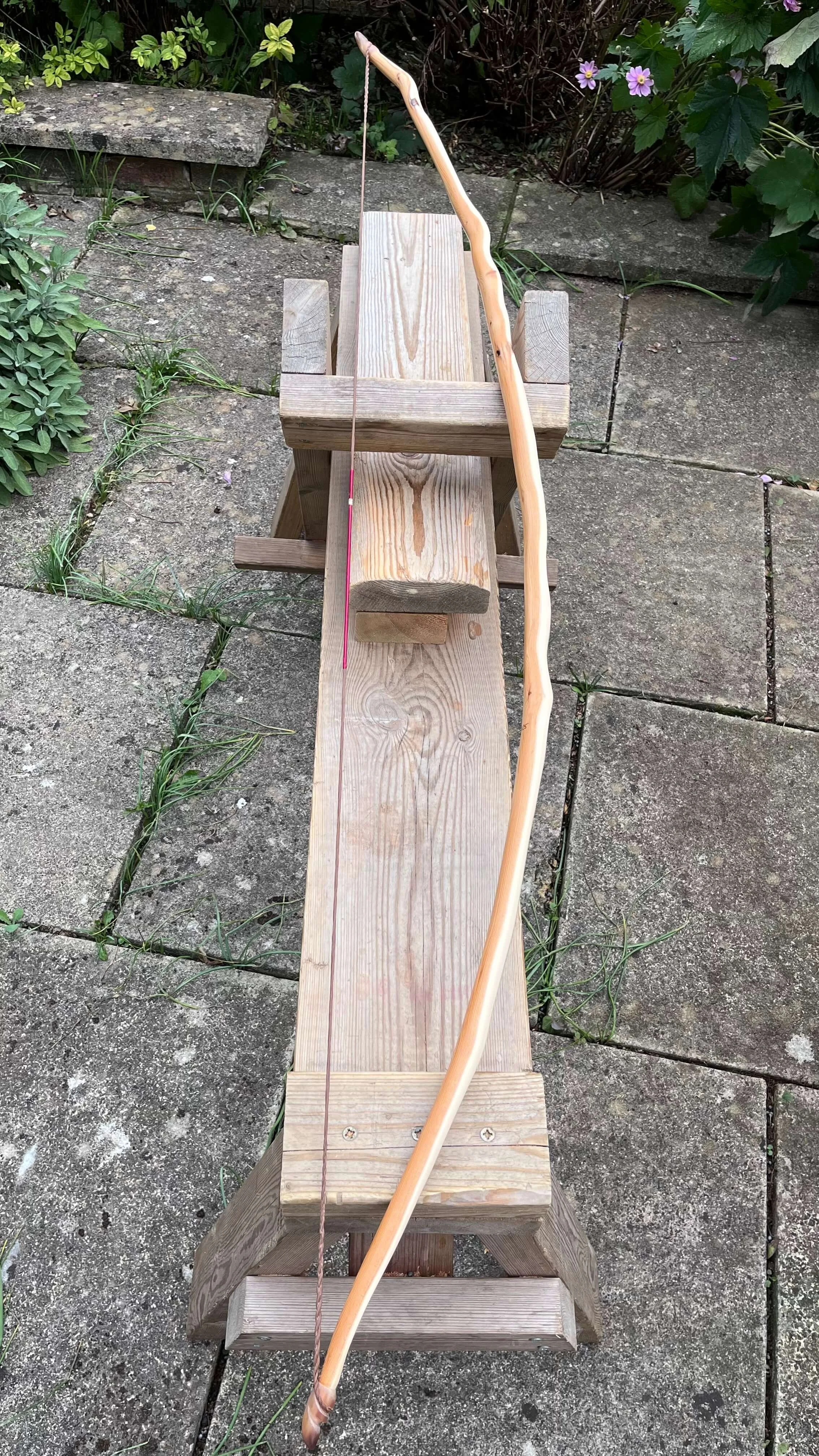 A strung English longbow resting on a shave horse to show off its arc and tiller.