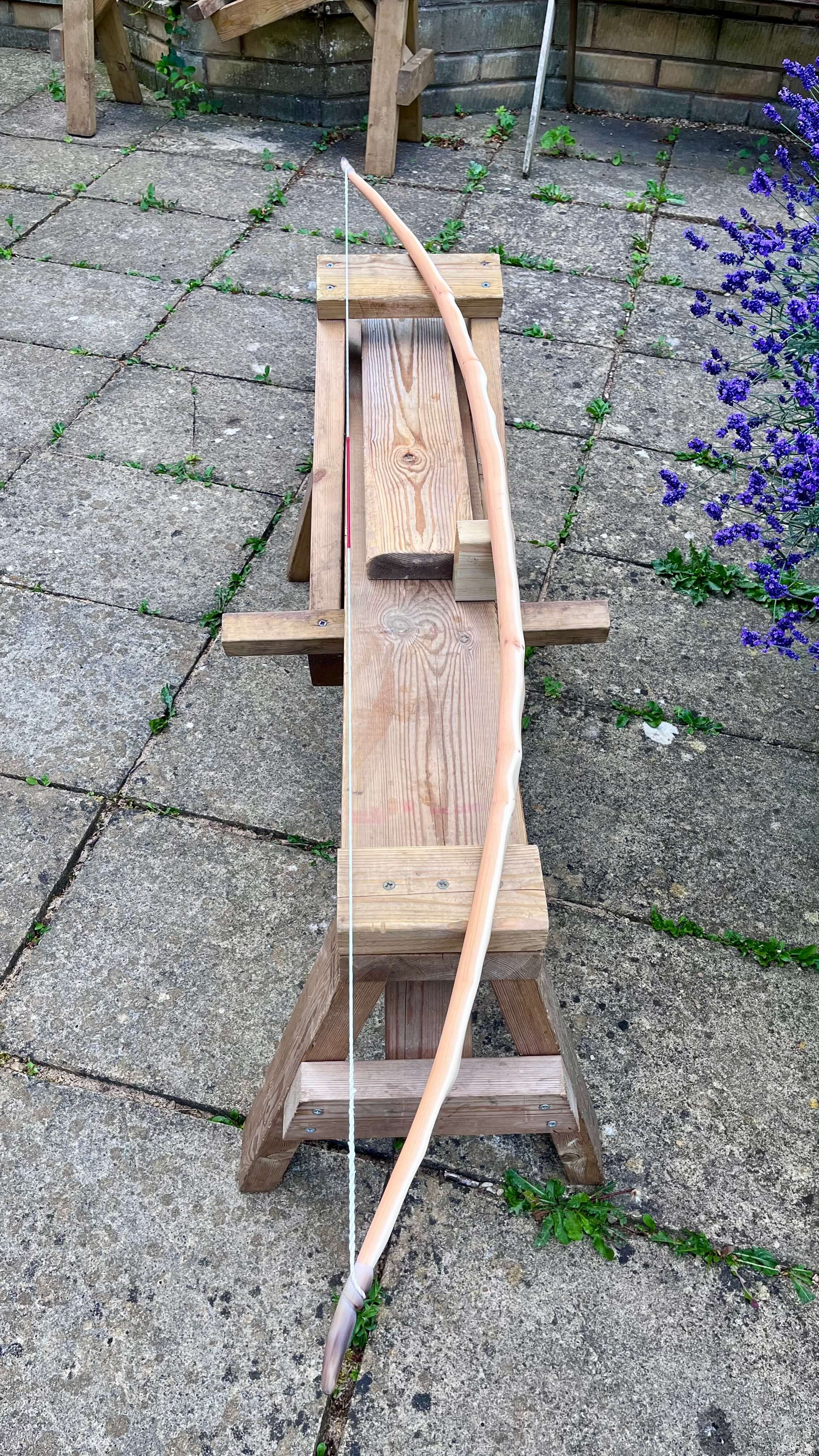 A strung English longbow resting on a shave horse to show off its arc and tiller.