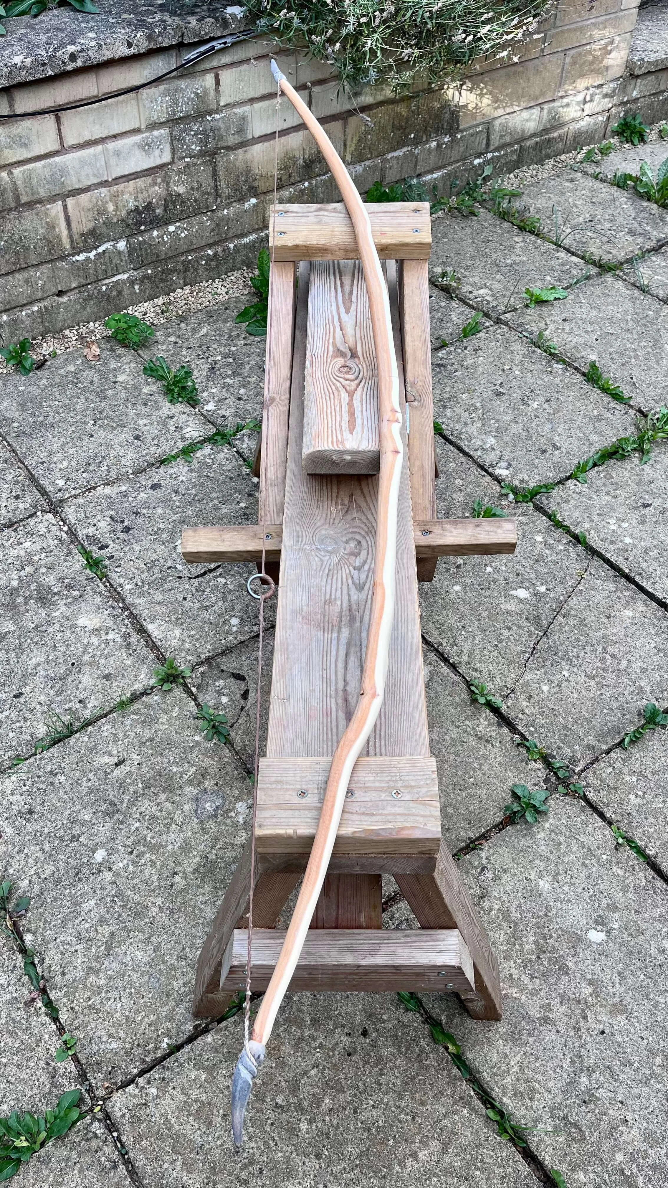 A strung English longbow resting on a shave horse to show off its arc and tiller.