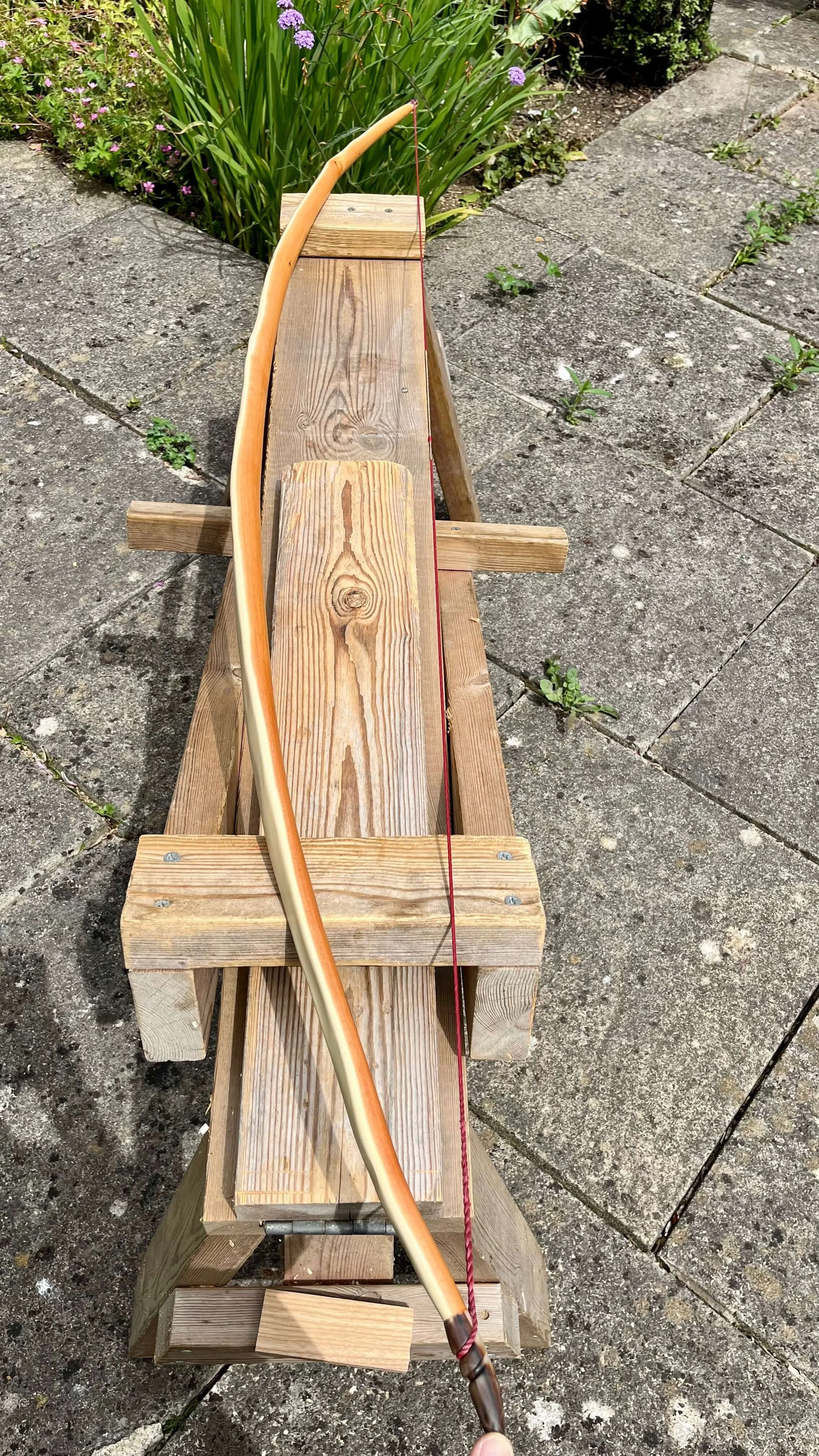 A strung English longbow resting on a shave horse to show off its arc and tiller.
