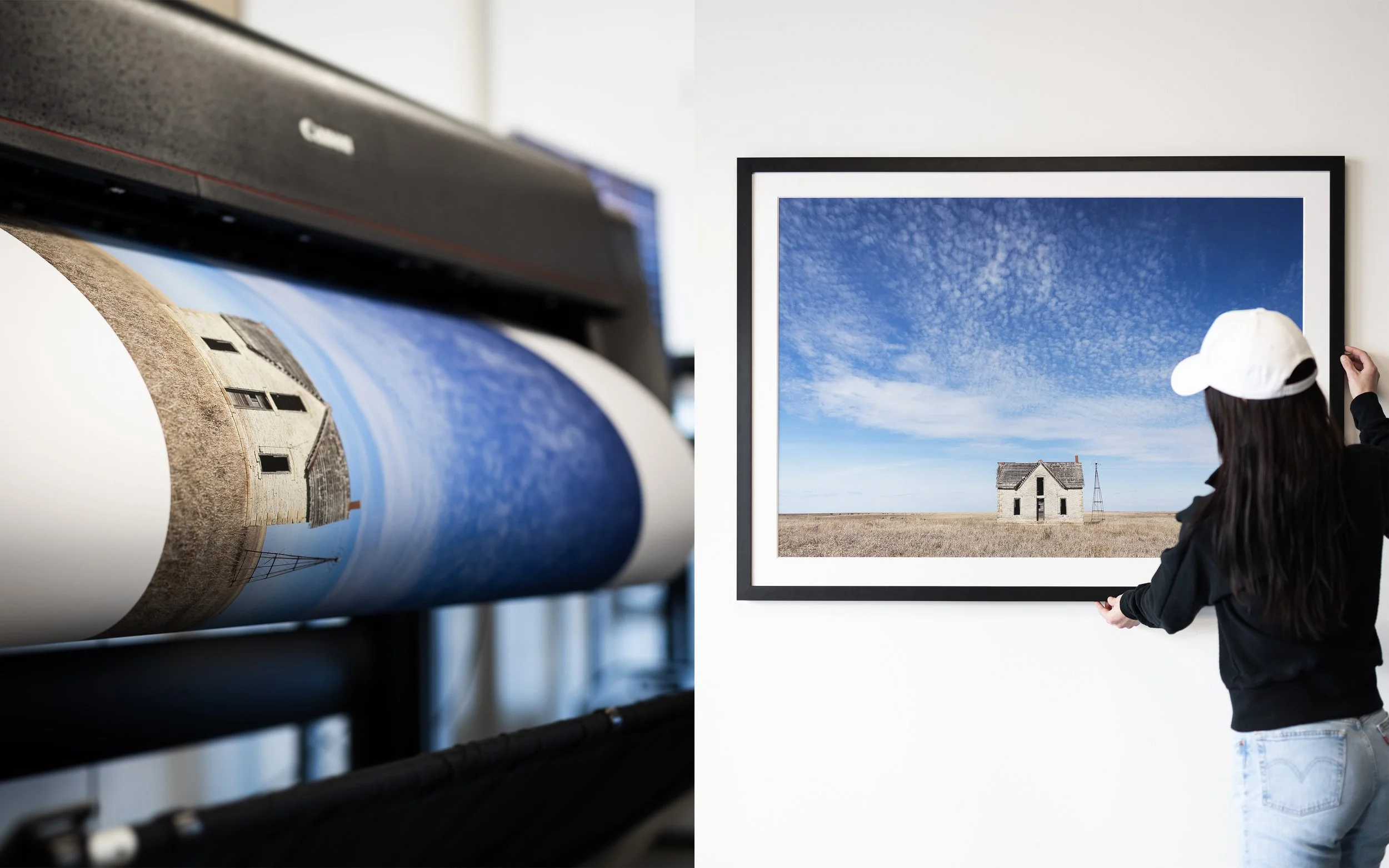 A woman adjusts a framed landscape photograph of a house in a field, under a bright blue sky with scattered clouds, in an art gallery.