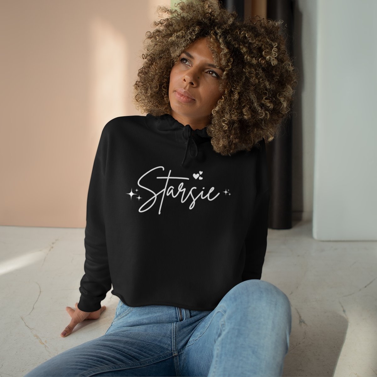Person with curly hair wearing a black hoodie with the word 'Starsie' sitting on the floor.