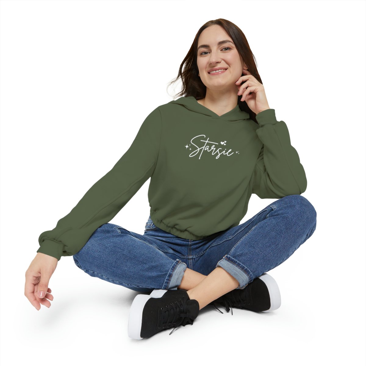 Person sitting cross-legged wearing a green hoodie with 'Starsie' printed on it and jeans, with a white background.
